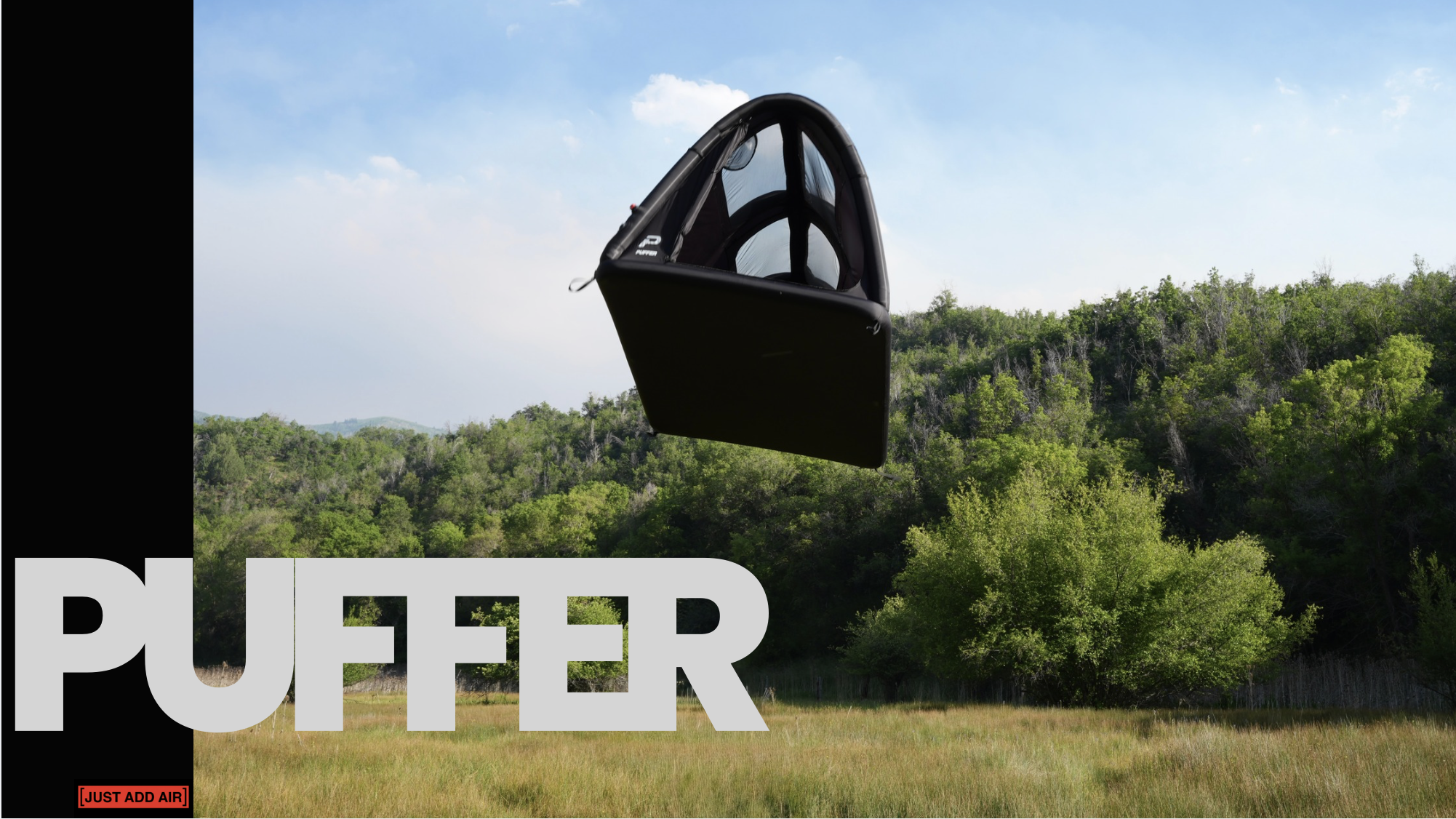 A black puffer tent  above a green forested landscape during daytime. The image includes a partial overlay of white text that says 'PUFFER' and a small red box with '[JUST ADD AIR]' in black text.