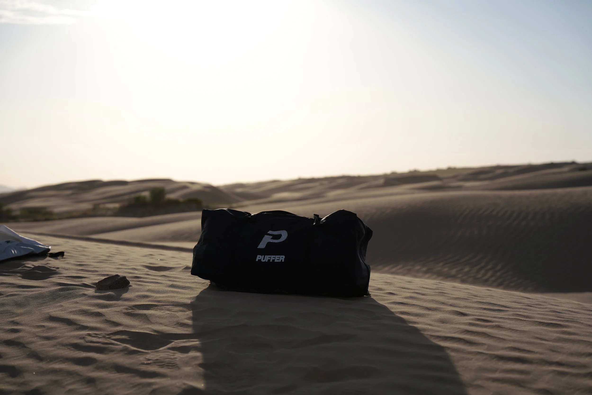 Sand dunes in a desert landscape with a black bag labeled 'PUFFER' in the foreground.