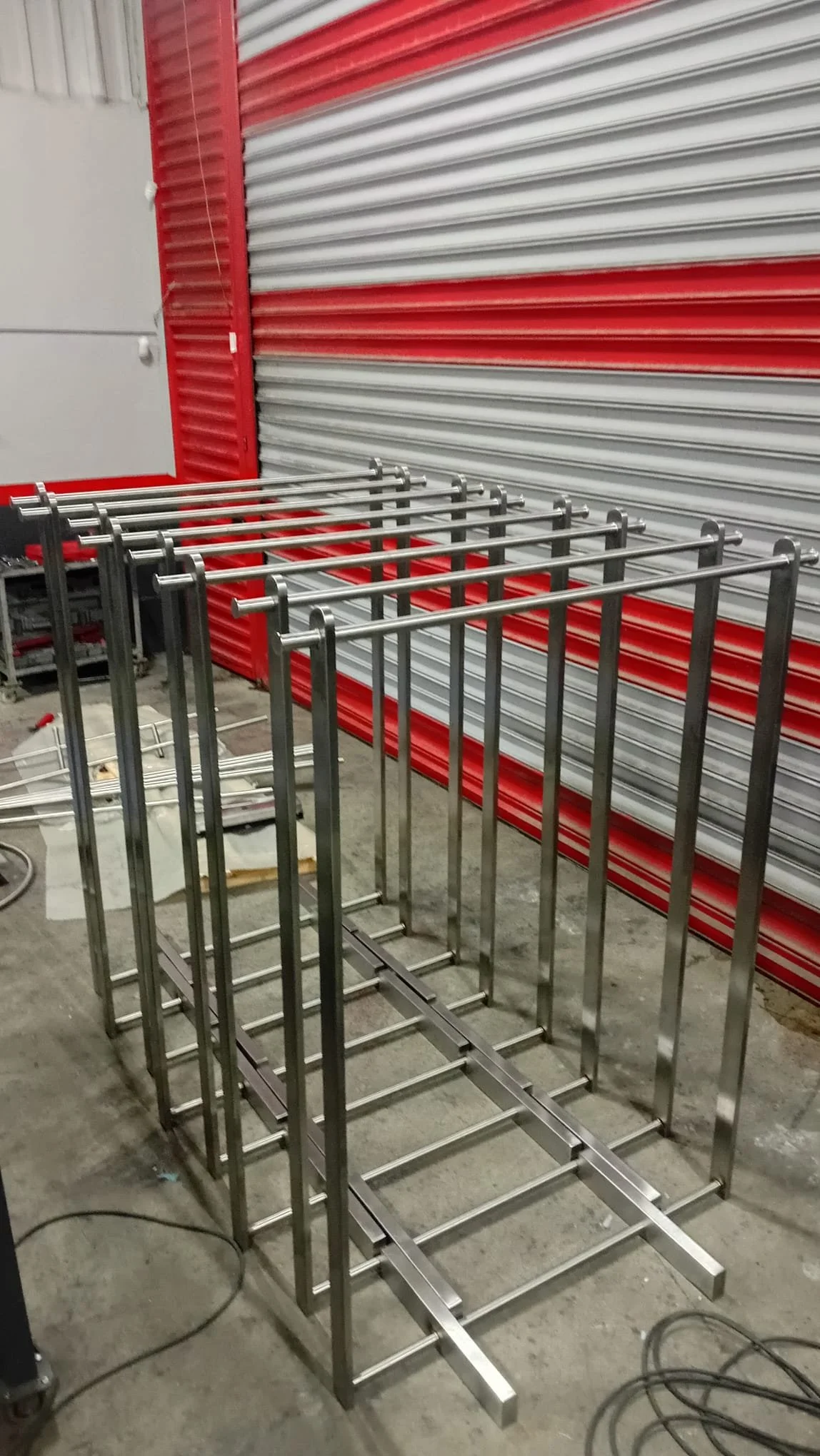 Metal frame structure being assembled in a workshop with a red and gray striped rolling door in the background.