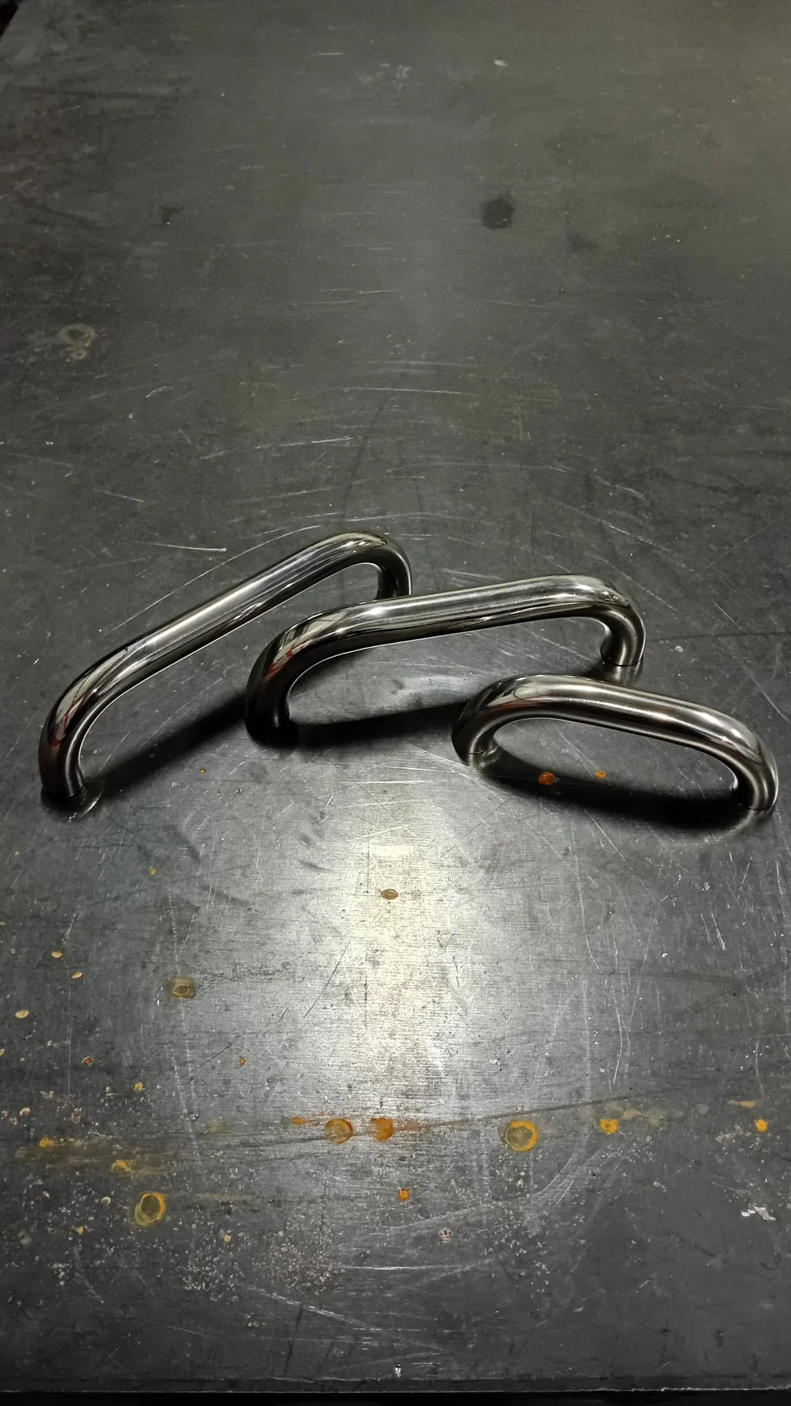 Three metal towel hooks placed on a black surface.