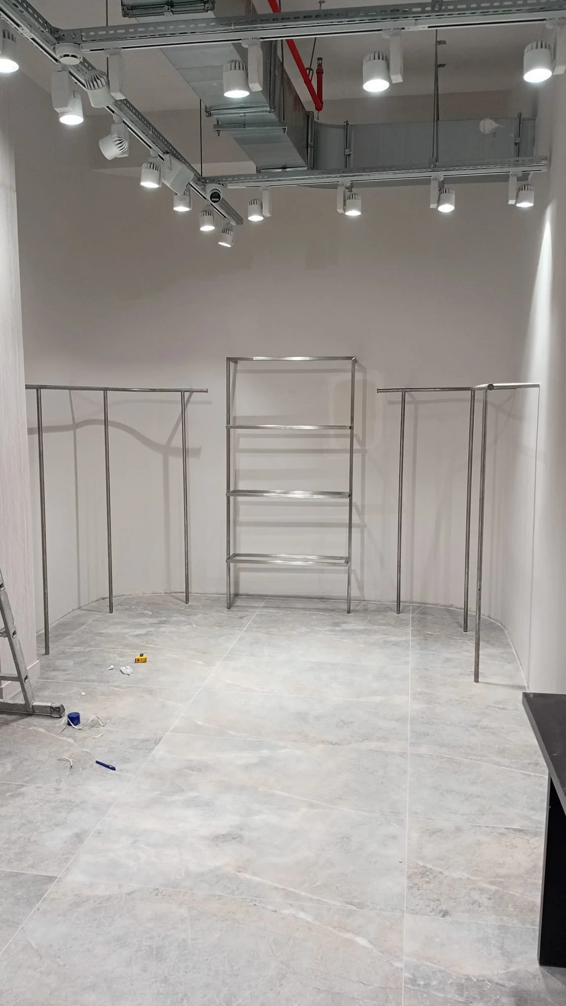 İçeride boş metal raflar ve ışıklandırma bulunan bir oda veya mağaza hazırlığı yapılıyor.