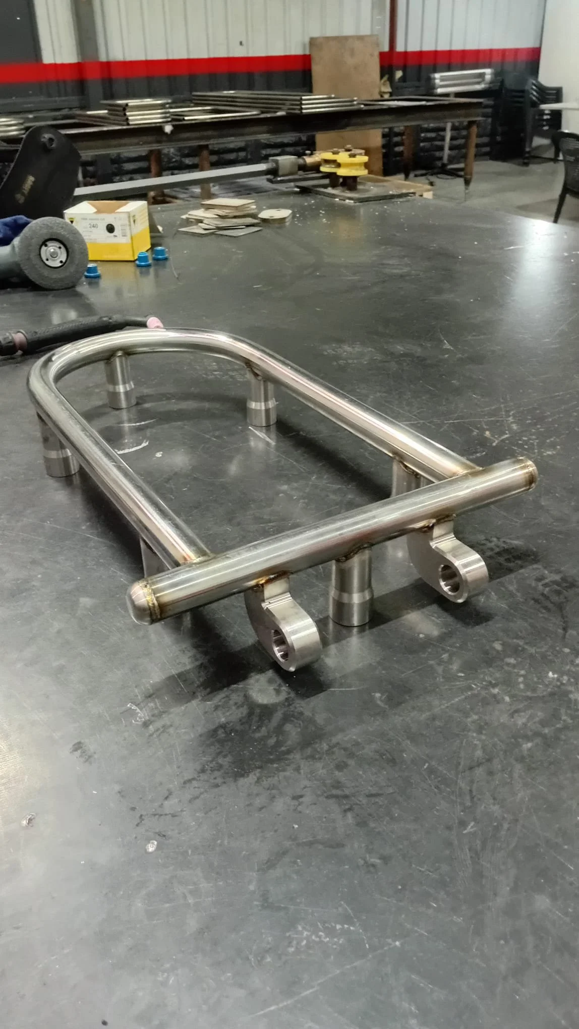 A metal frame structure on a black worktable in a workshop, with various tools and materials in the background.