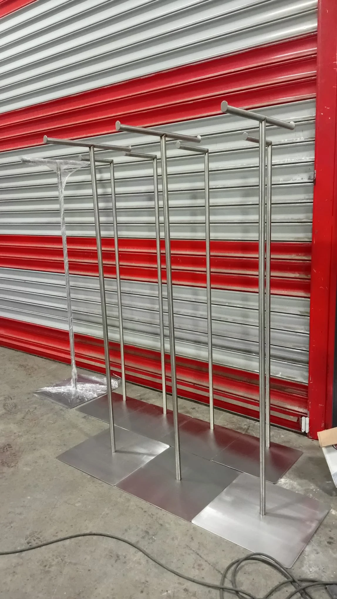 Gümüş renkli metal asksılar ve standlar, arkada kırmızı ve gri kaplama kepenkler ve beton zemin ile fabrika veya depo ortamında.