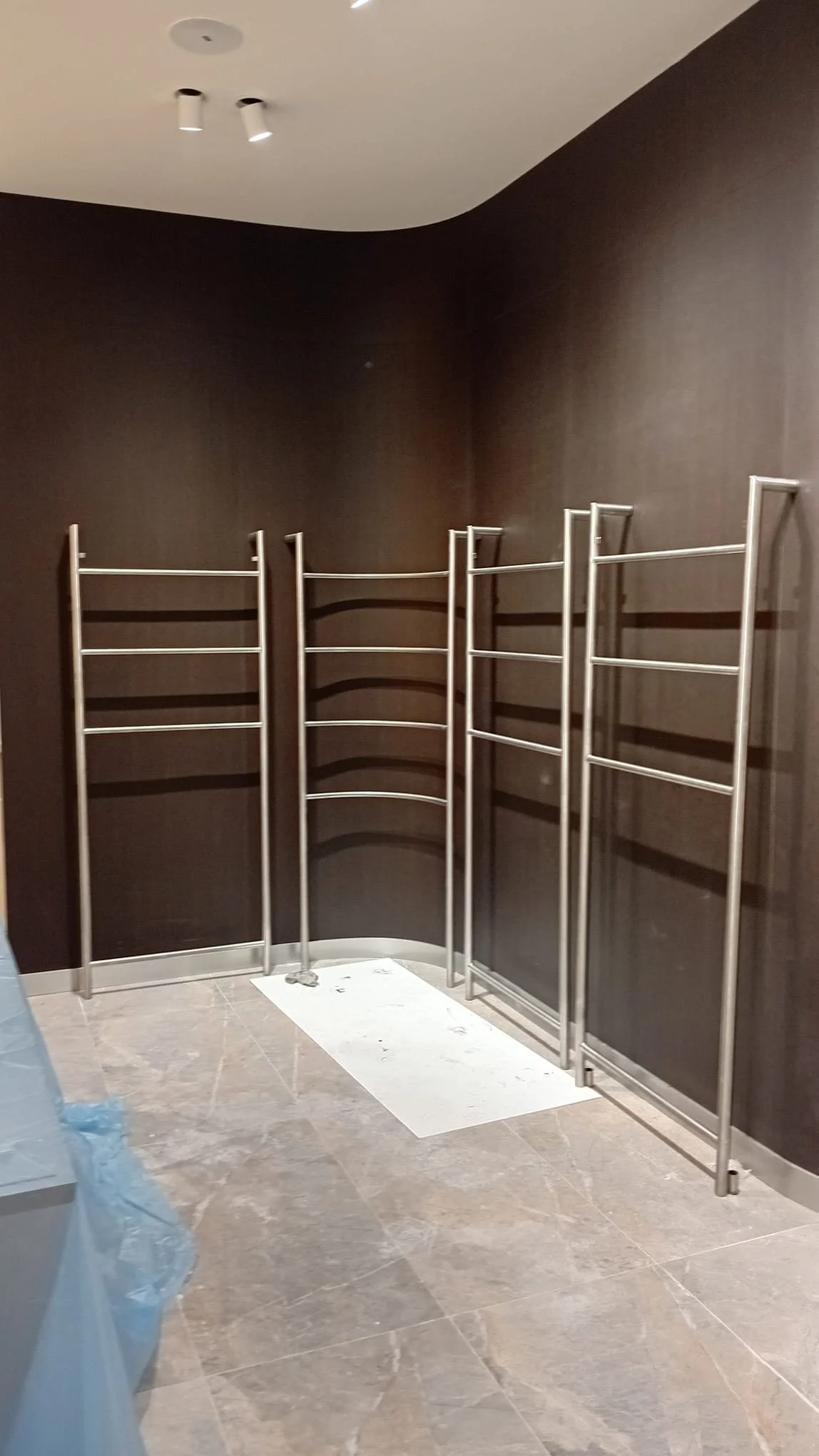Metal shelves or racks are installed against a dark wall, with a white mat or cloth on the floor underneath. The room appears to be under construction or renovation.