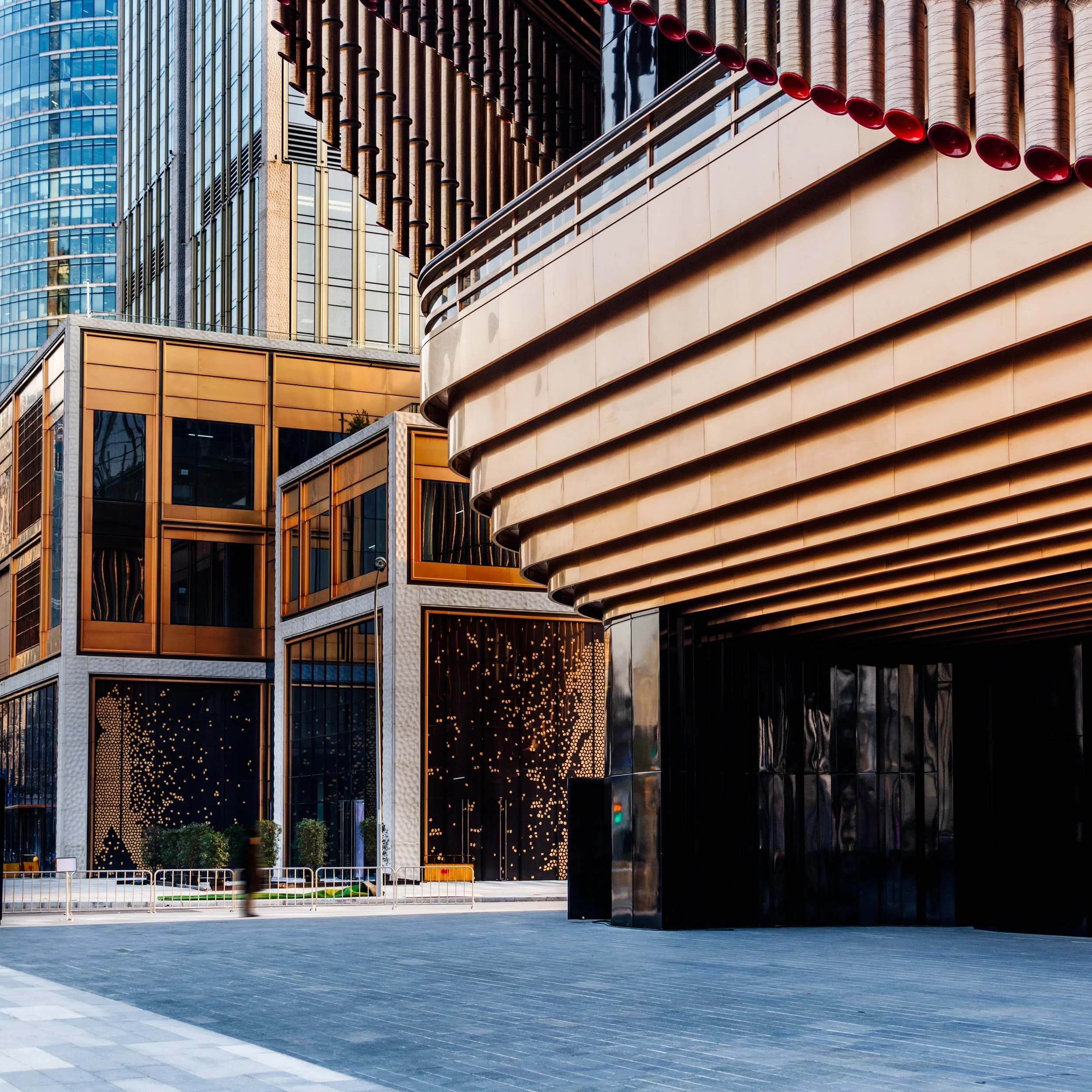 Modern urban buildings with glass facades and intricate architectural designs, featuring a curved metallic structure and a glass-fronted office building.