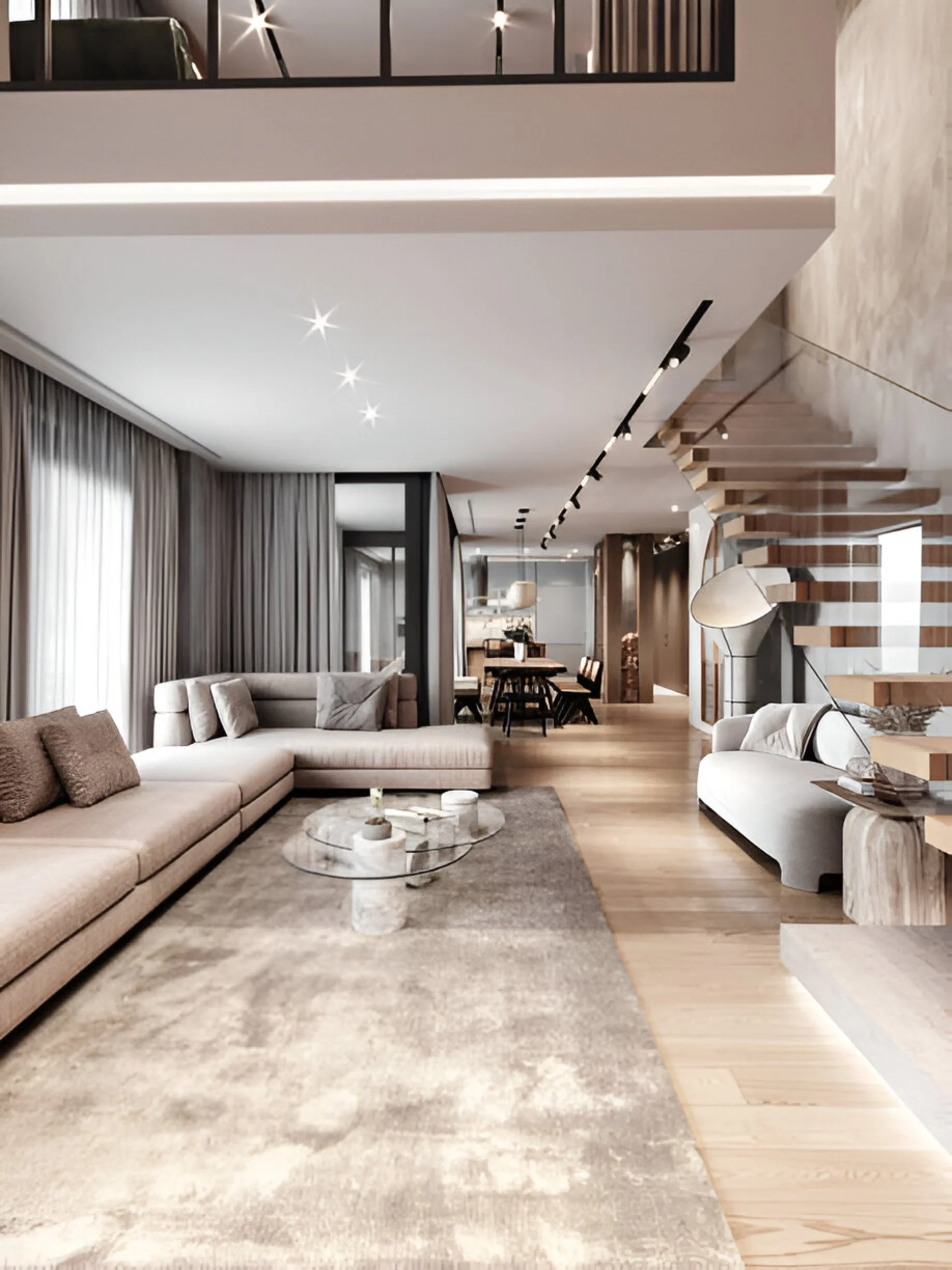 Modern living room with large beige sectional sofa, glass coffee table, and a muted color palette. Curtains, built-in lighting, wooden staircase, and a dining area in the background.