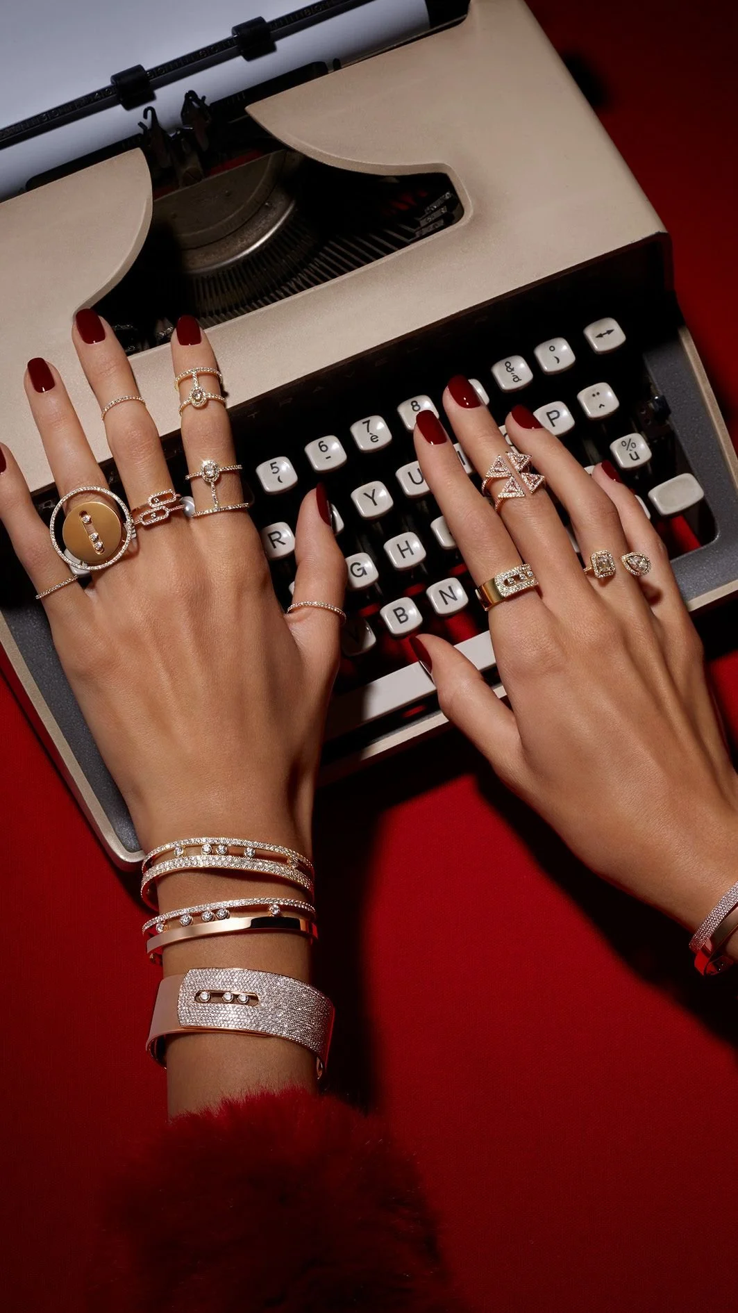 Hands with multiple rings and bracelets typing on vintage typewriter, red background.