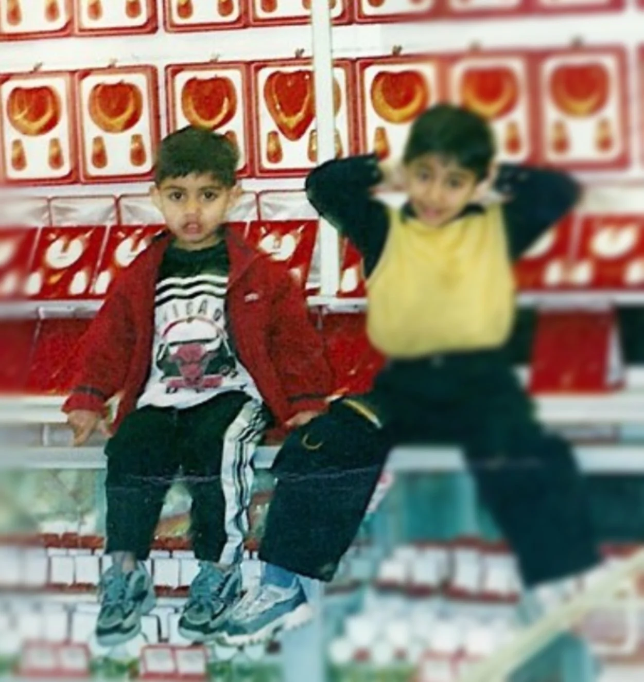 Two young boys sitting on a bench in front of a wall with a red and white pattern.