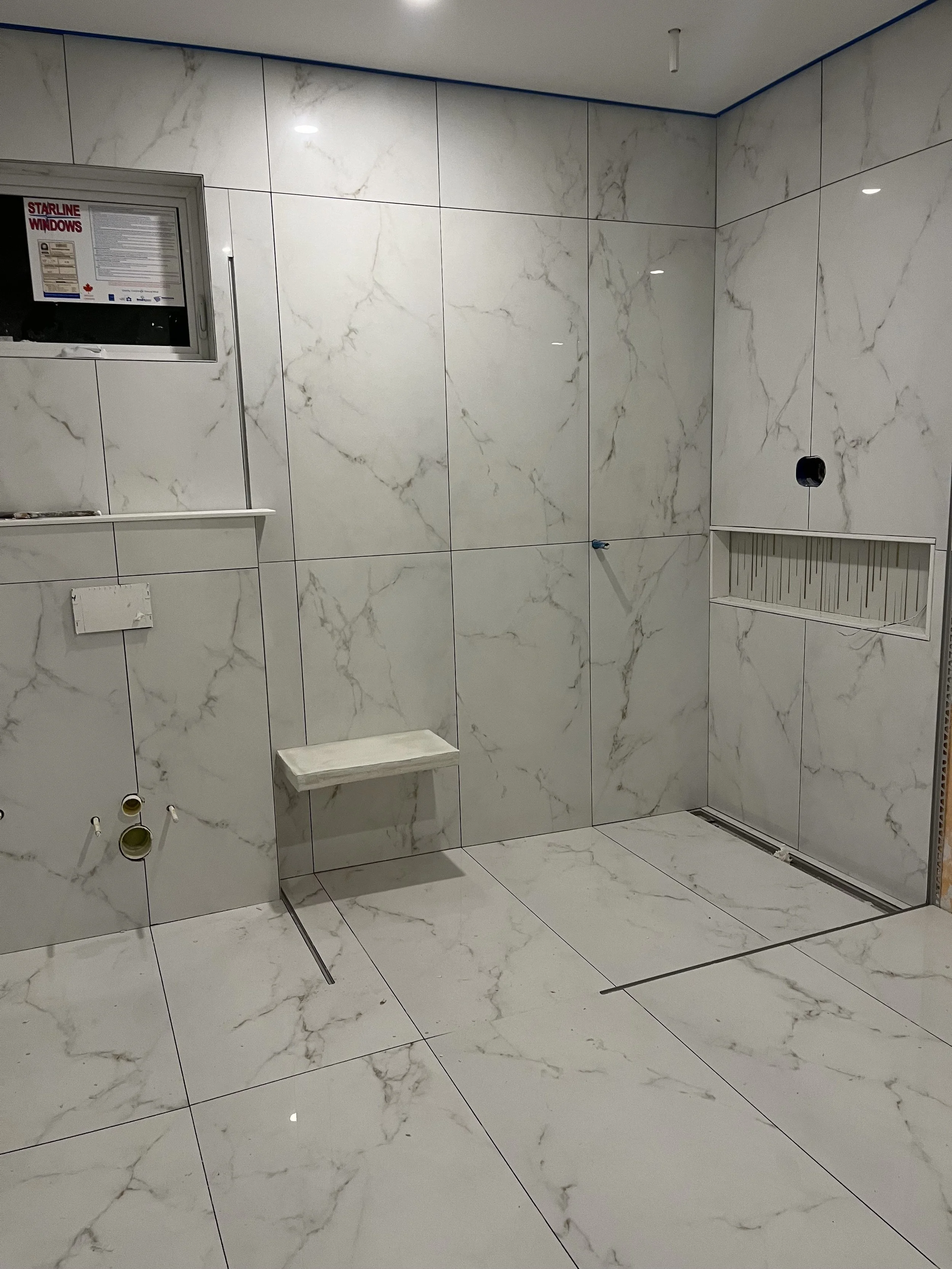 Curbless marble-look porcelain shower with built-in bench, linear drain, and recessed niche