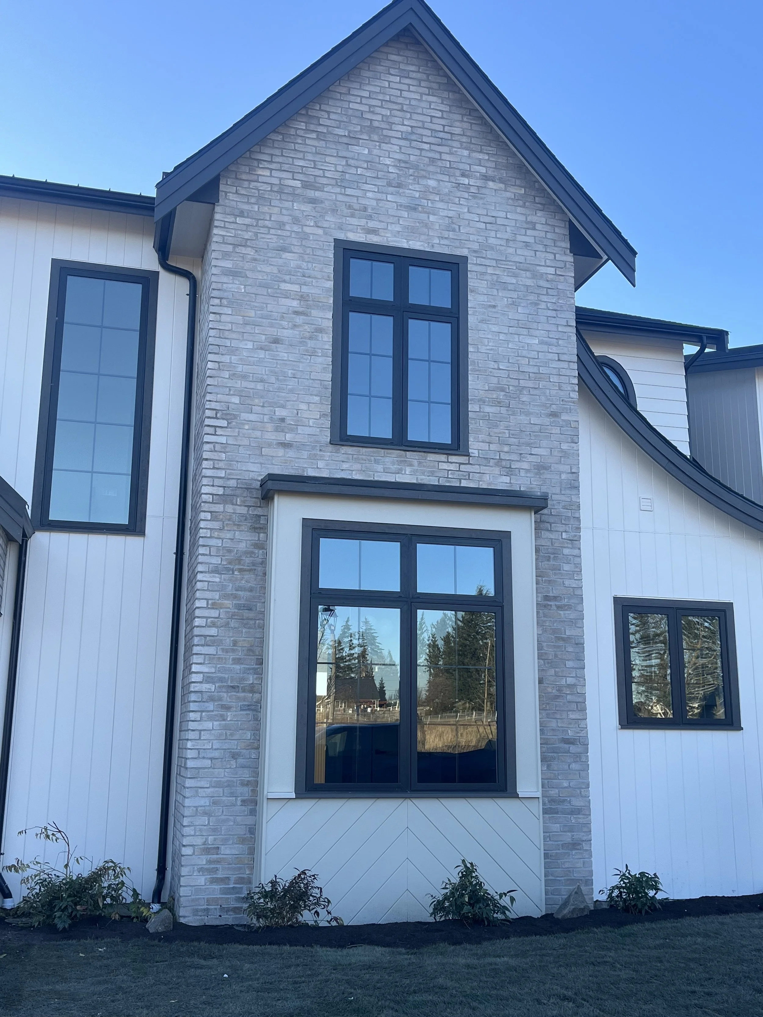 Custom two-story home in Bellingham with white board-and-batten siding, brick accent gable, and black-framed windows