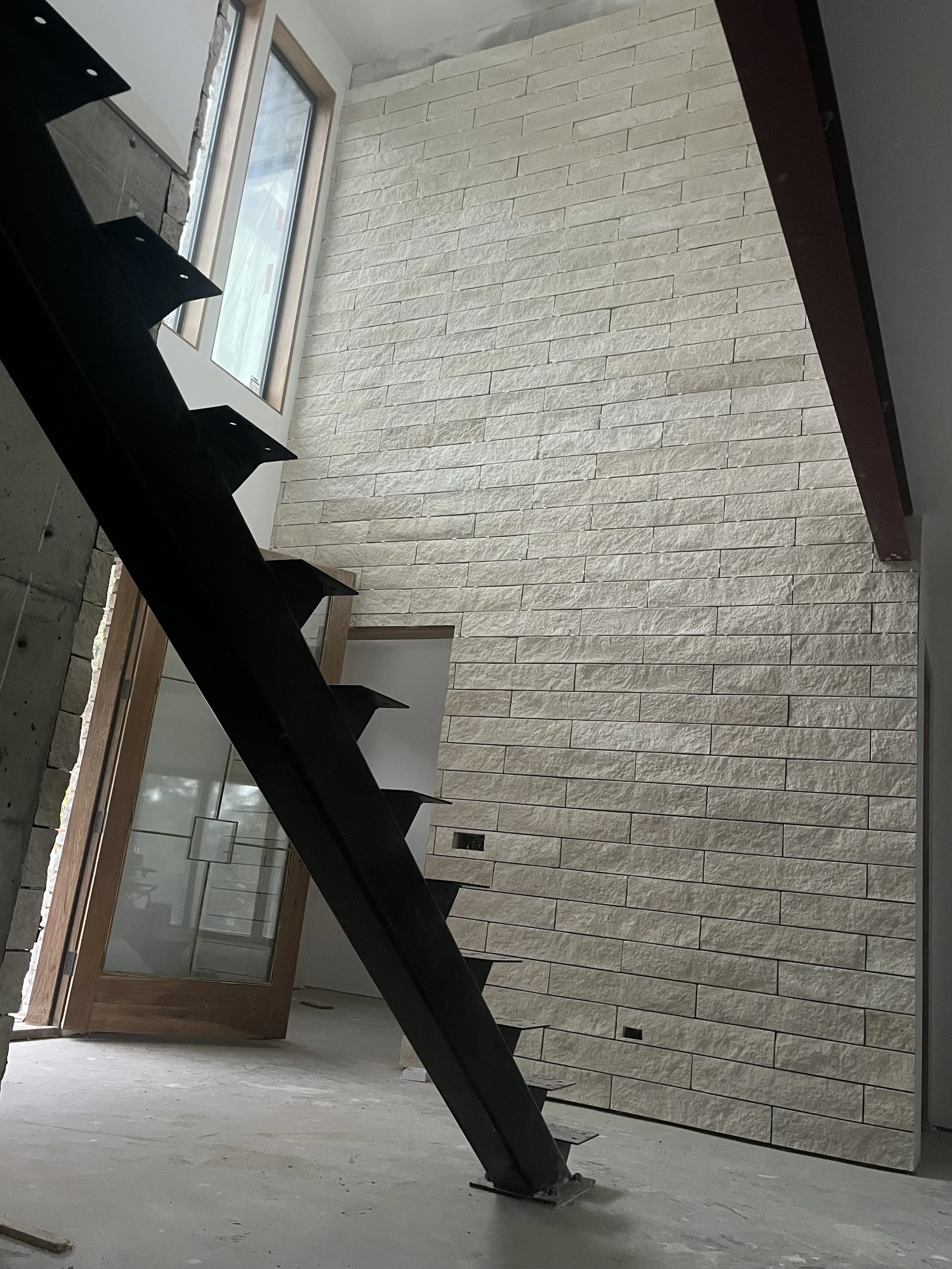 Stacked stone feature wall with black steel open-riser staircase in new Bellingham home