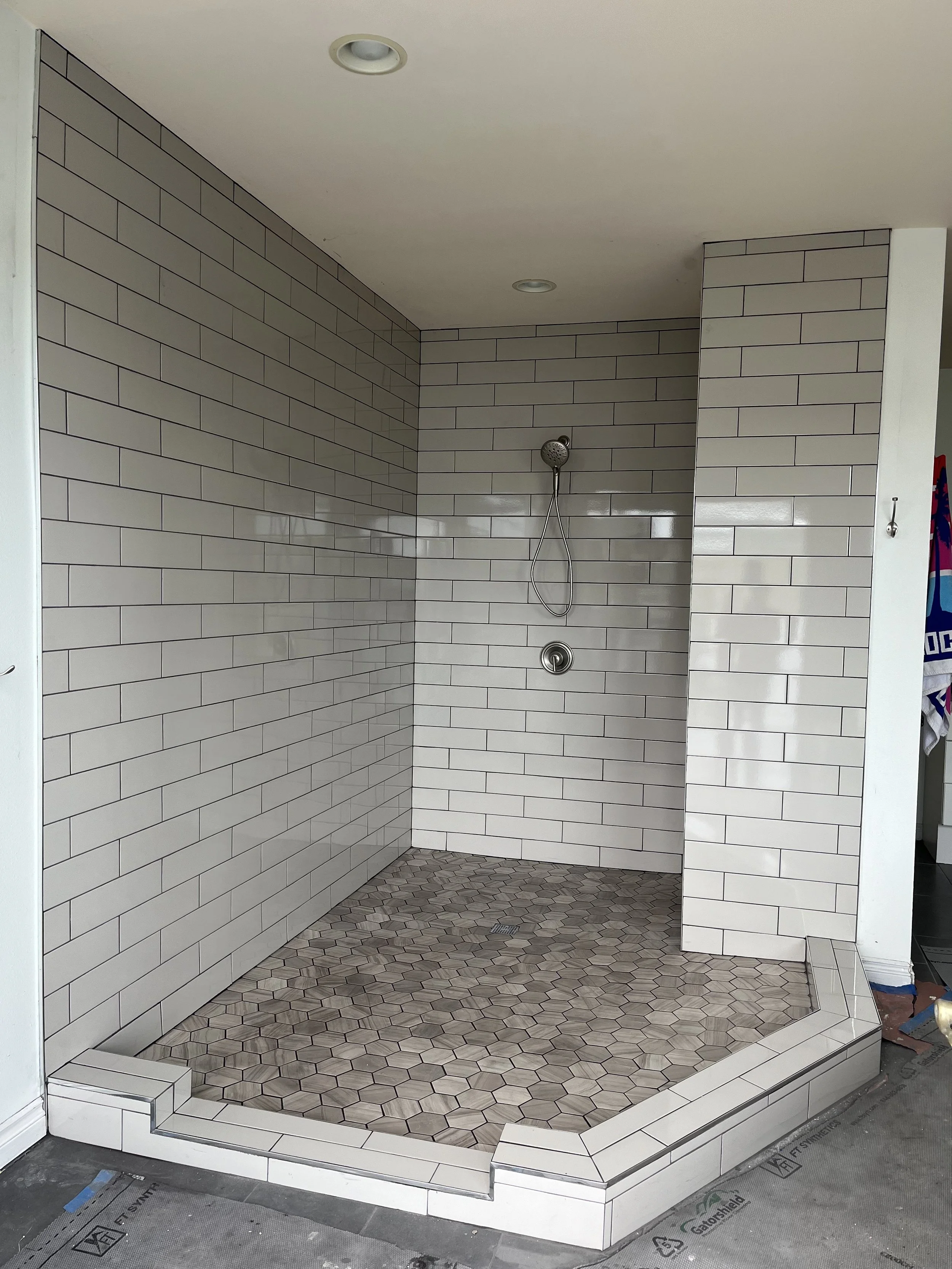 Walk-in tile shower with white subway tile walls and hexagon floor