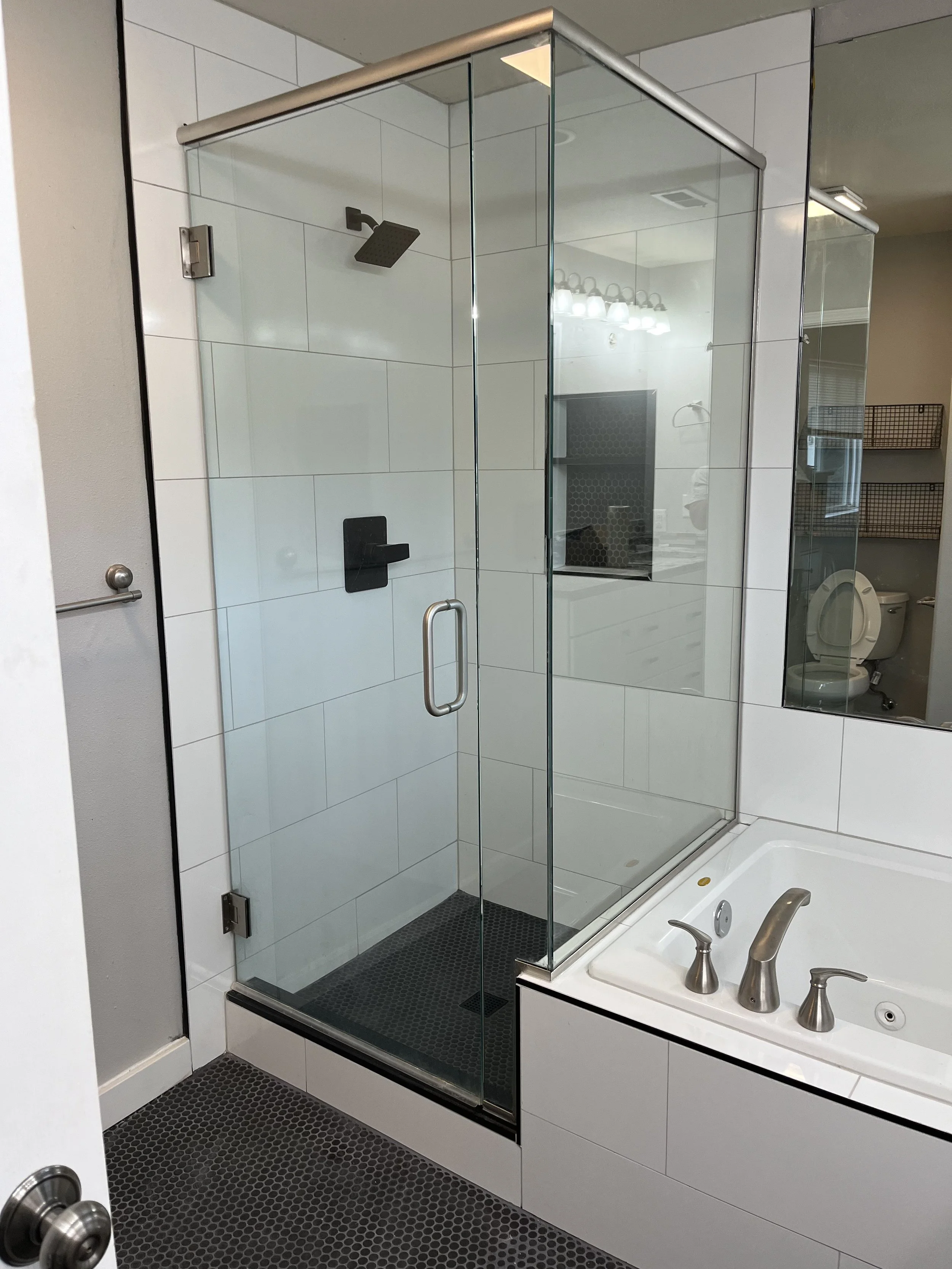 Whatcom County bathroom remodel featuring glass-enclosed shower with white tile surround, black pebble floor, and adjoining soaking tub