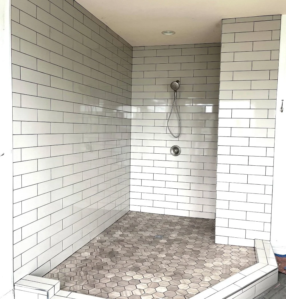 White subway tile shower with a pebble stone floor and recessed niche