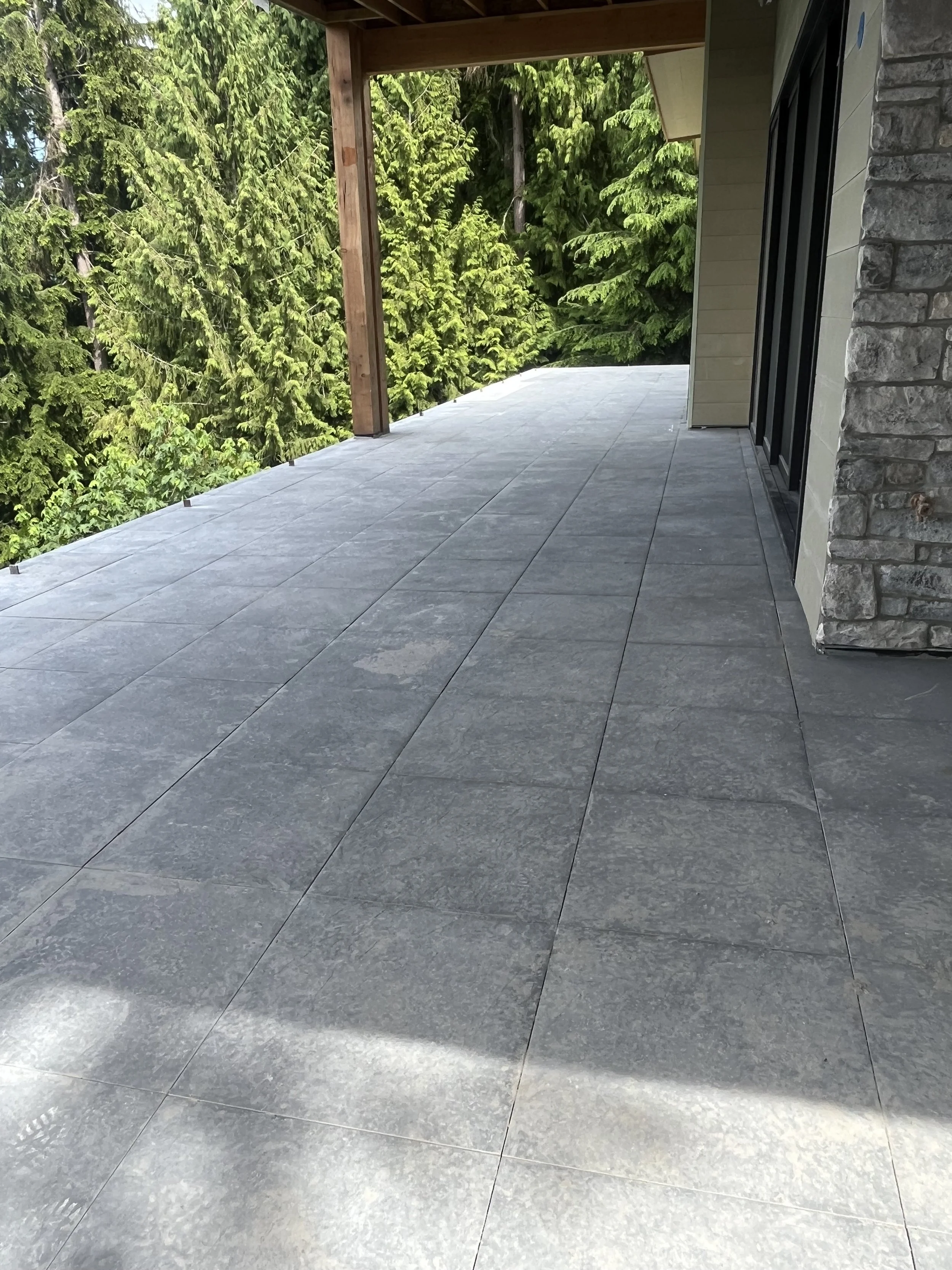 Covered outdoor patio in Ferndale with large-format gray porcelain pavers overlooking forest
