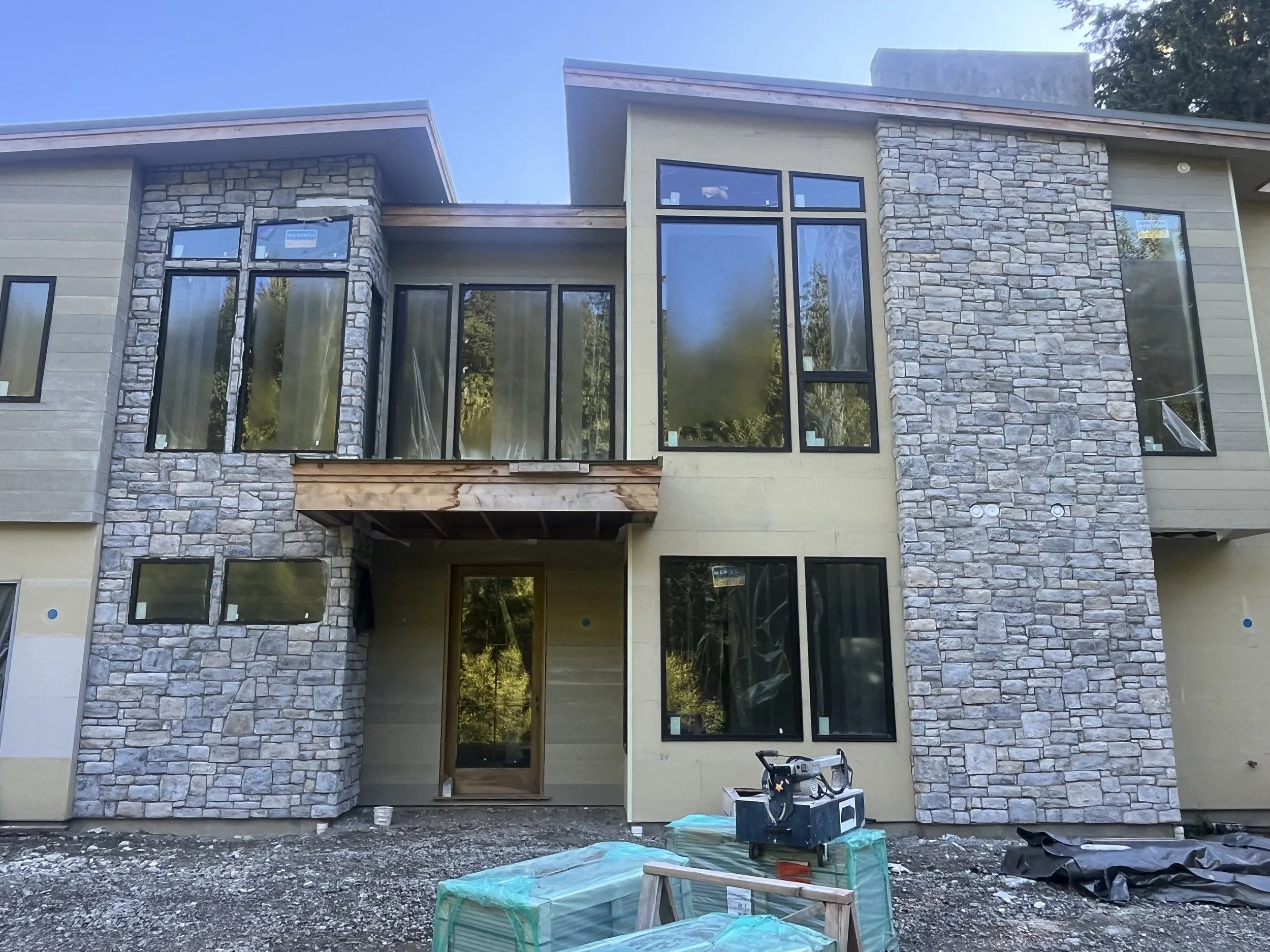 Modern two-story home with stone veneer columns and cedar beam entry under construction in Whatcom County