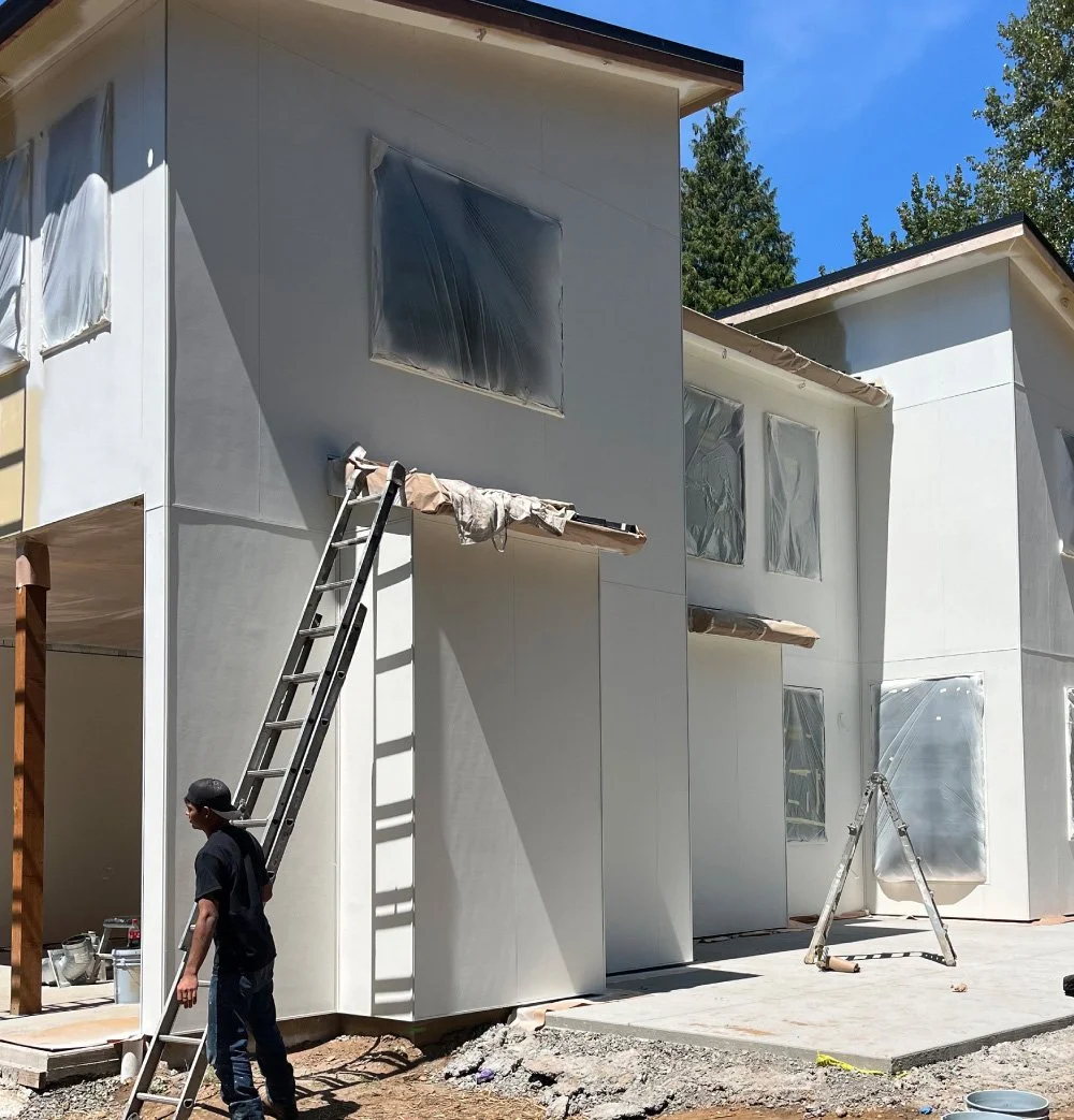 Painter on a ladder applying a fresh coat to the exterior of a cream-colored house