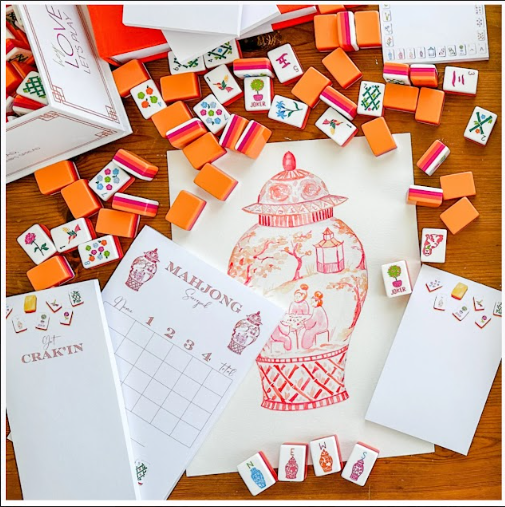 Board game pieces, mahjong tiles, and handwritten notes surrounding a drawing of a snow globe on a wooden table.