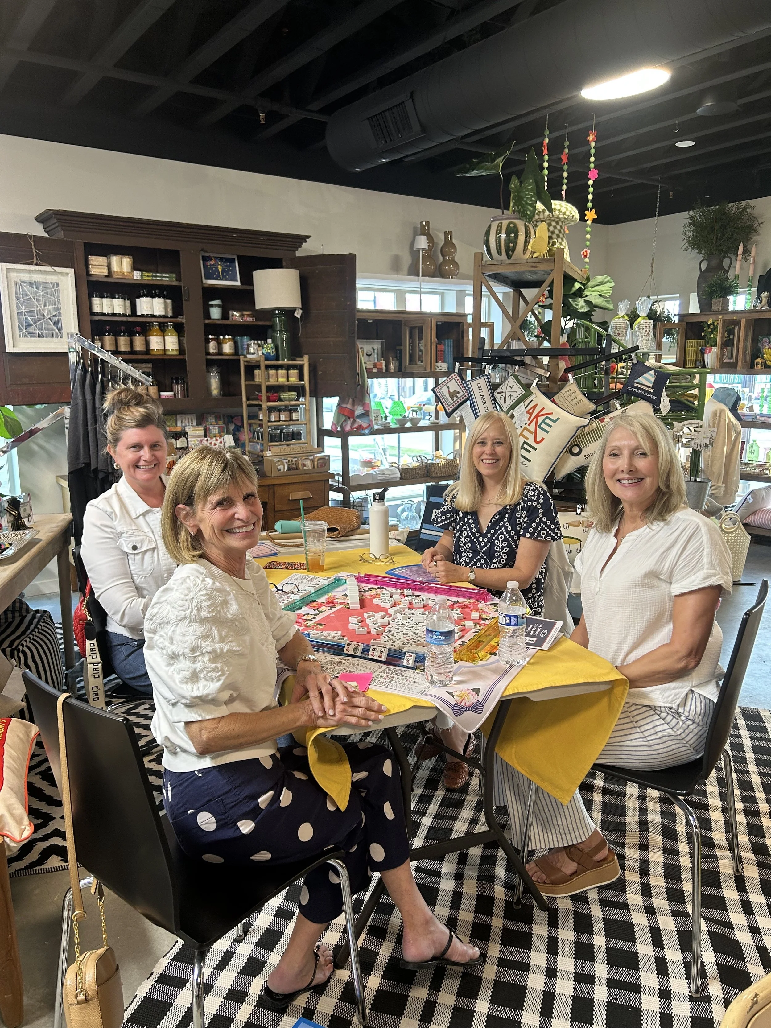 Four women sitting around a table playing a board game in a decorated shop or café.