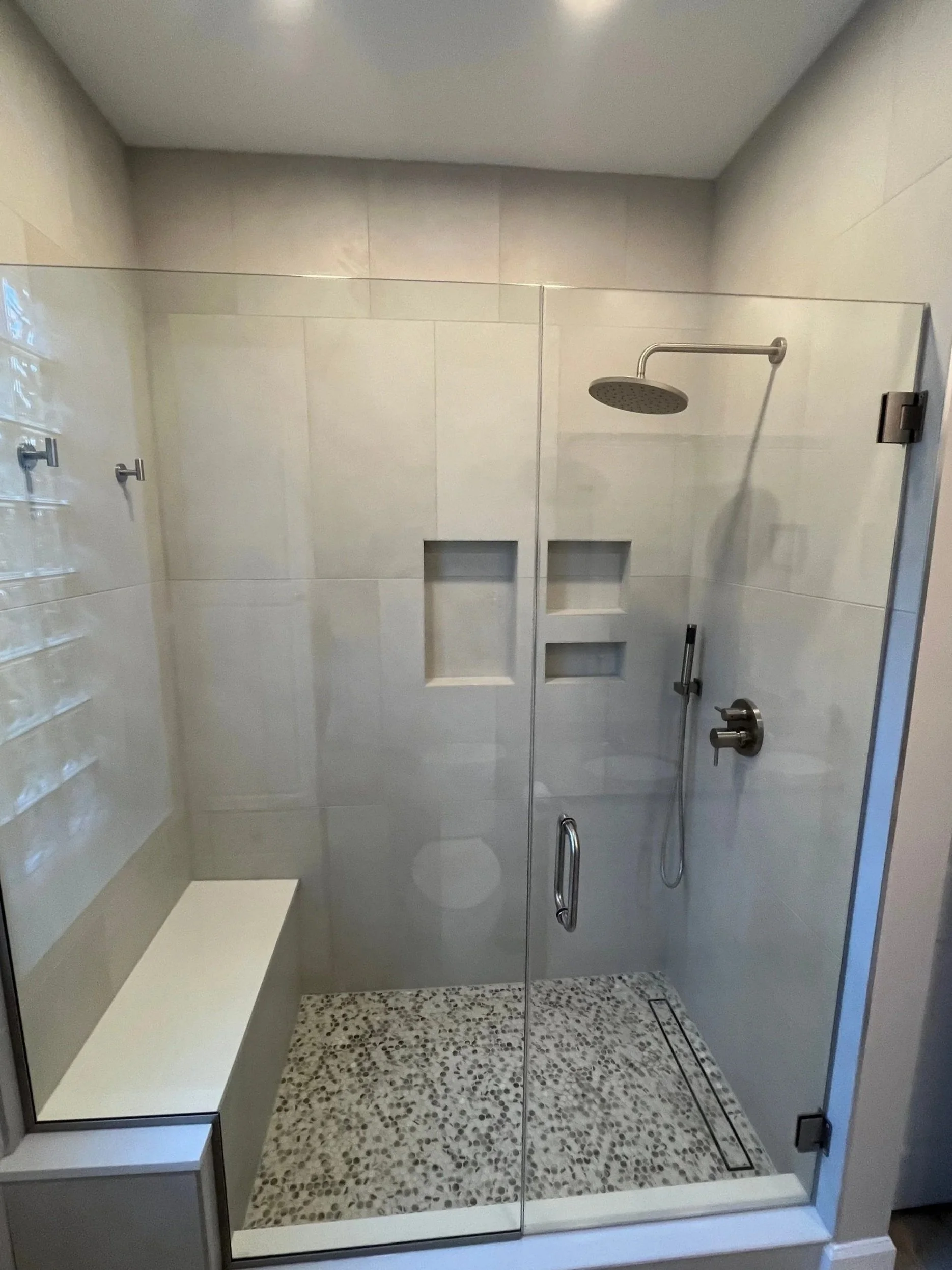 Primary bath shower renovation with stone-looking porcelain tile in vertical stack installation pattern with in-shower bench and towel hooks, frameless shower glass, rain shower system and penny tile floor with tile-in linear drain
interior designer 