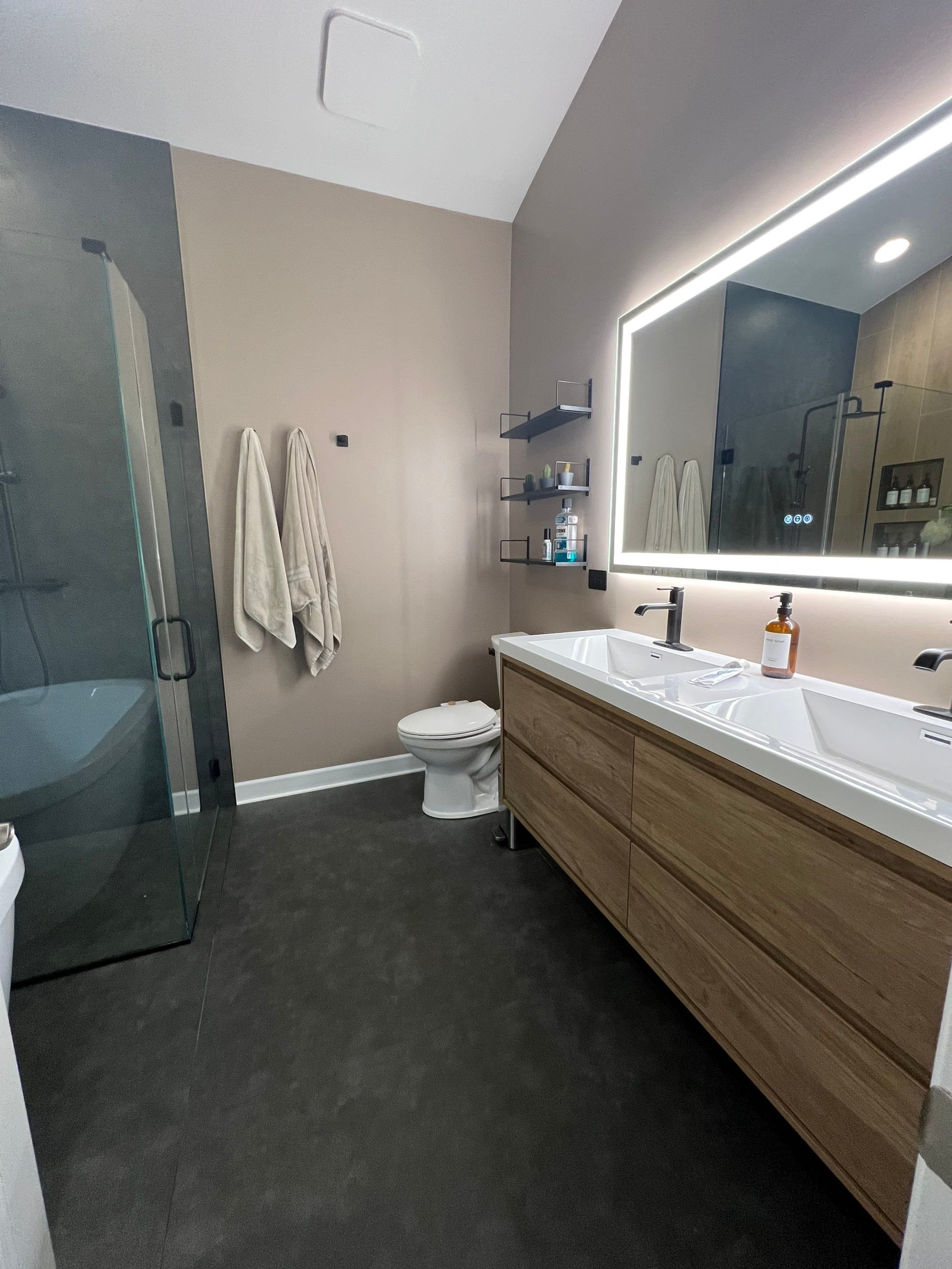 primary bath interior design with large format tile in wood-look pattern and cement color, freestanding bathtub, recessed niches wtih lighting, seamless shower with hidden drain, rain shower system, floating vanity, LED lit mirror, vaulted ceiling
in