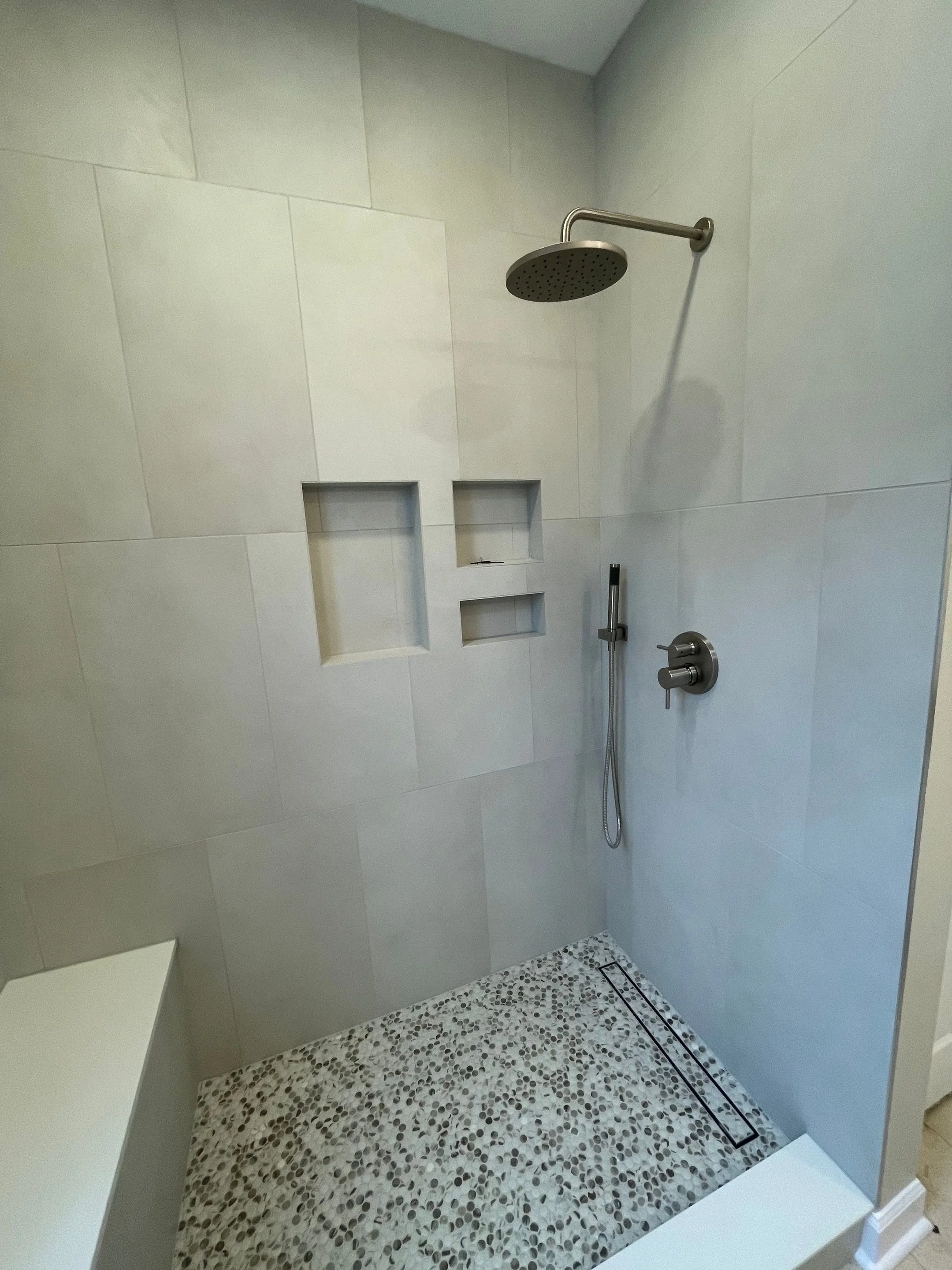 Primary bath shower renovation with stone-looking porcelain tile in vertical stack installation pattern with in-shower bench and towel hooks, frameless shower glass, rain shower system and penny tile floor with tile-in linear drain
interior designer 