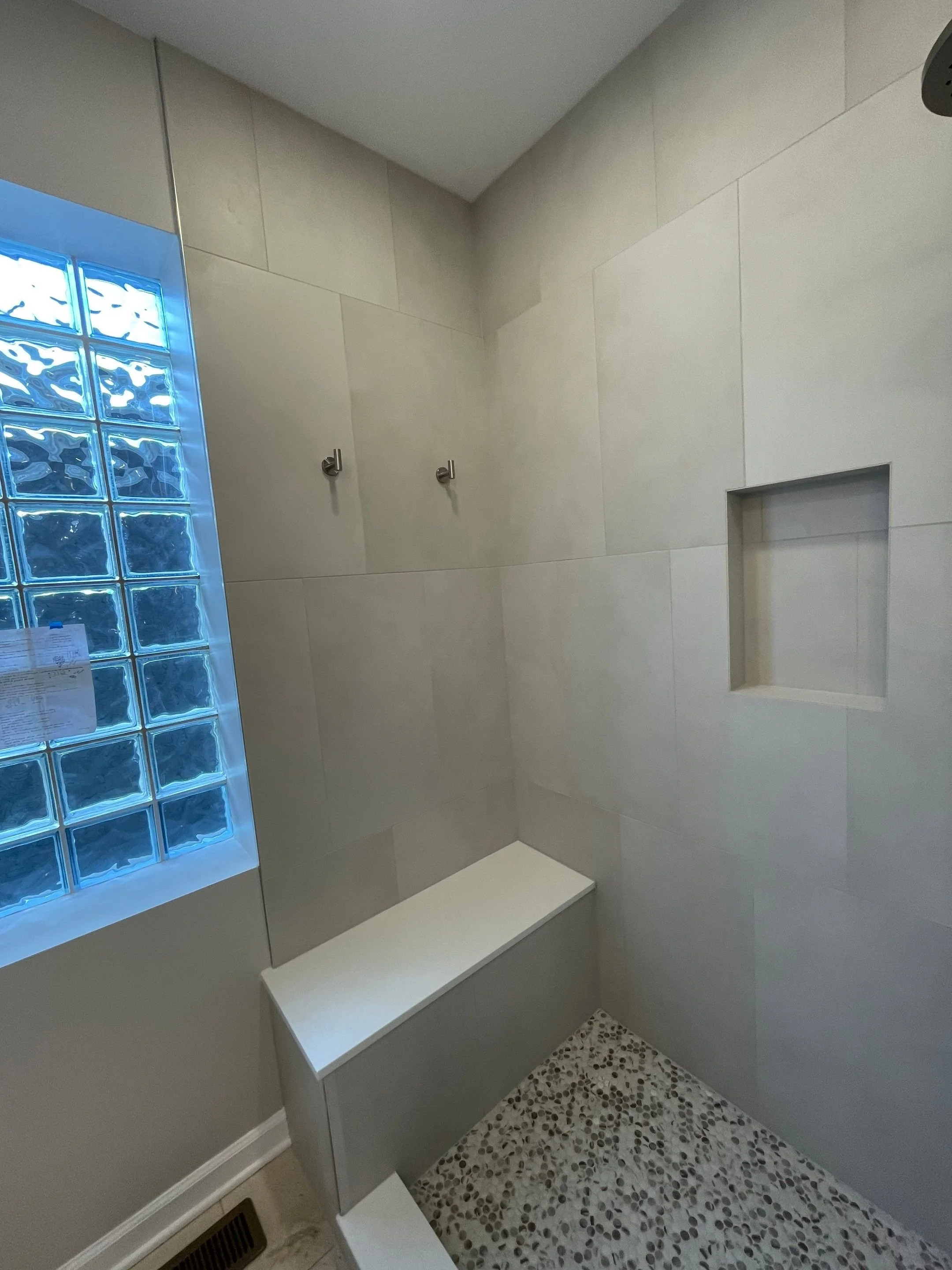 Primary bath shower renovation with stone-looking porcelain tile in vertical stack installation pattern with in-shower bench and towel hooks, frameless shower glass, rain shower system and penny tile floor with tile-in linear drain
interior designer 