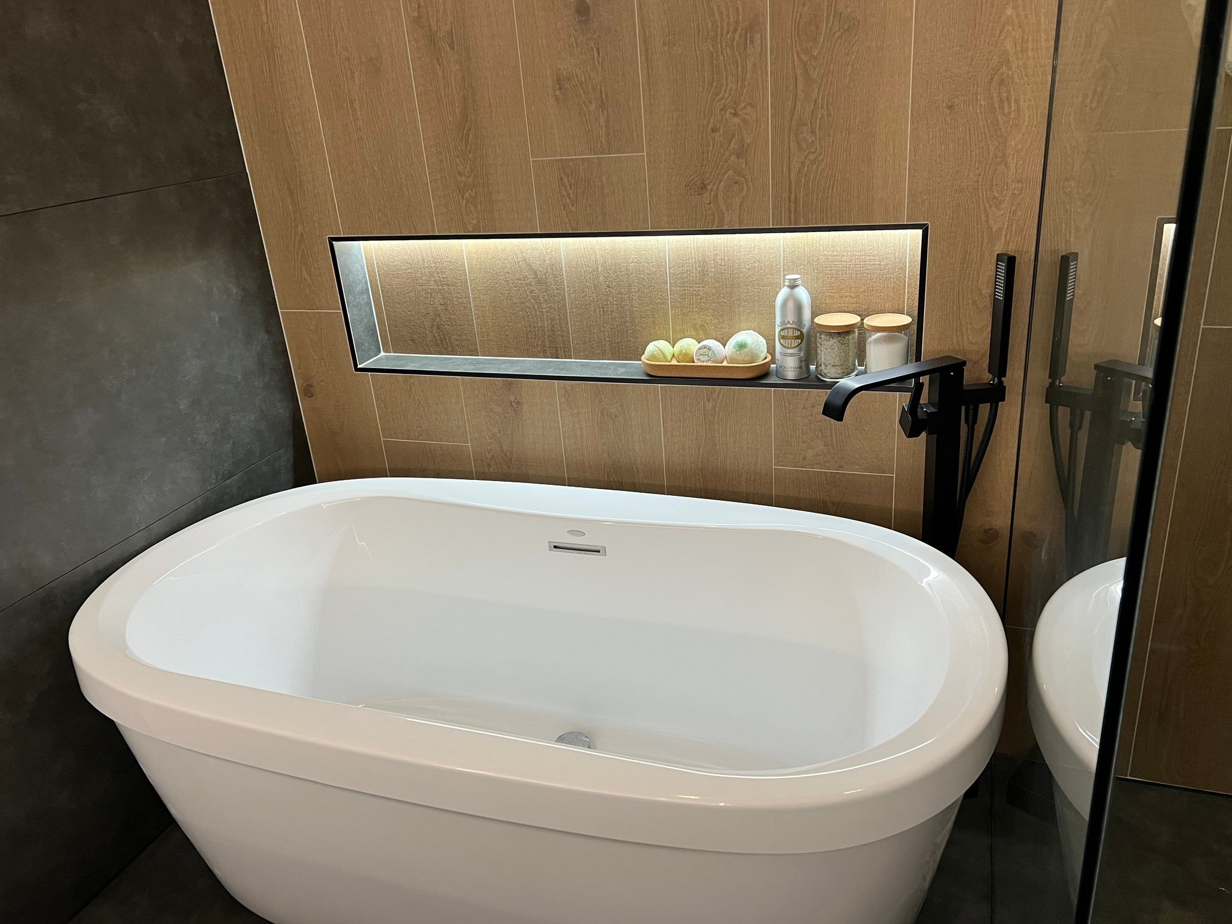 primary bath interior design with large format tile in wood-look pattern and cement color, freestanding bathtub, recessed niches wtih lighting, seamless shower with hidden drain, rain shower system, floating vanity, LED lit mirror, vaulted ceiling
in