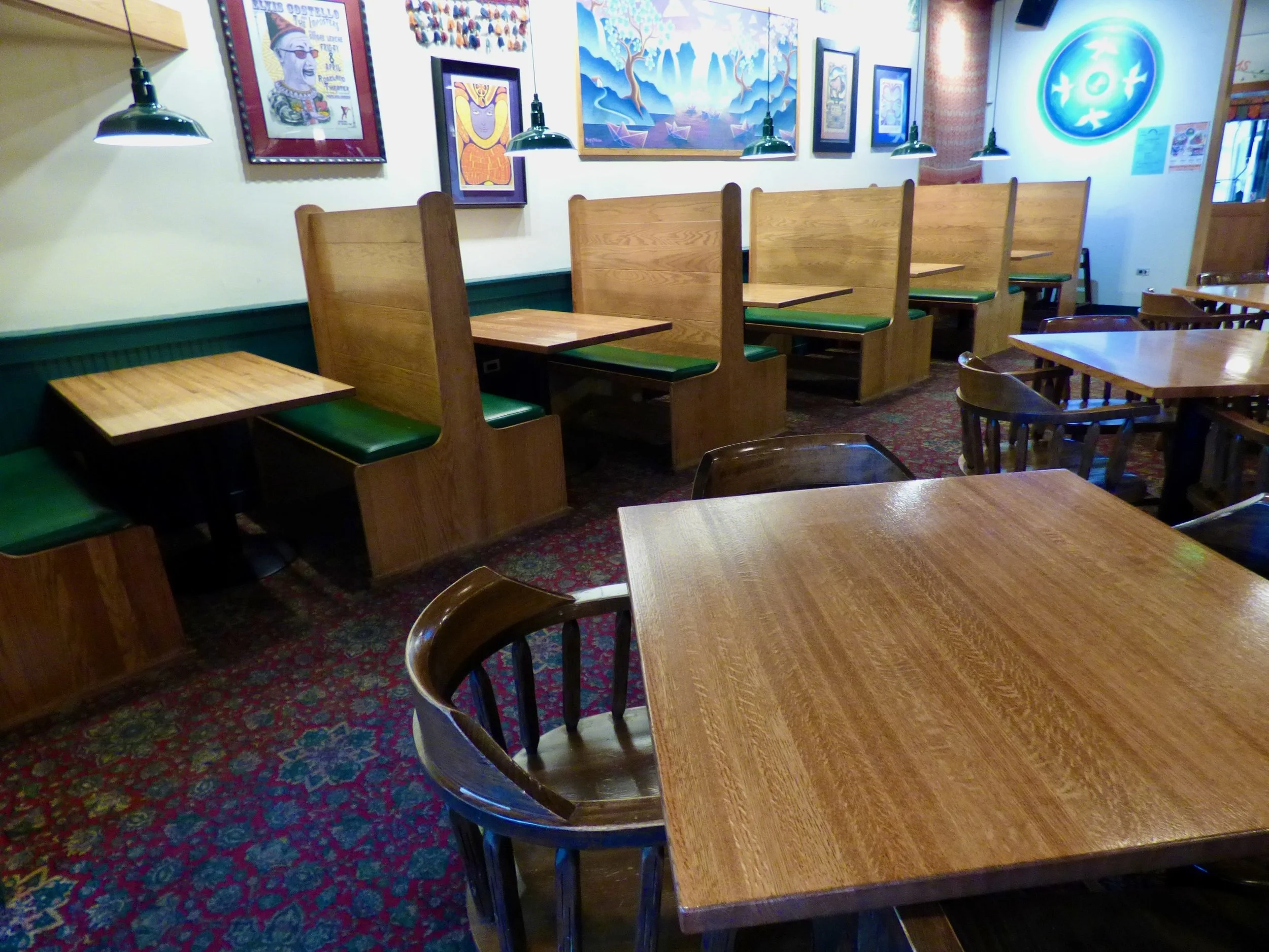 Empty restaurant with wooden tables and booths, framed artwork on the wall, green pendant lighting, and a decorative illuminated sign at Vine Street Pub, Denver, CO.
