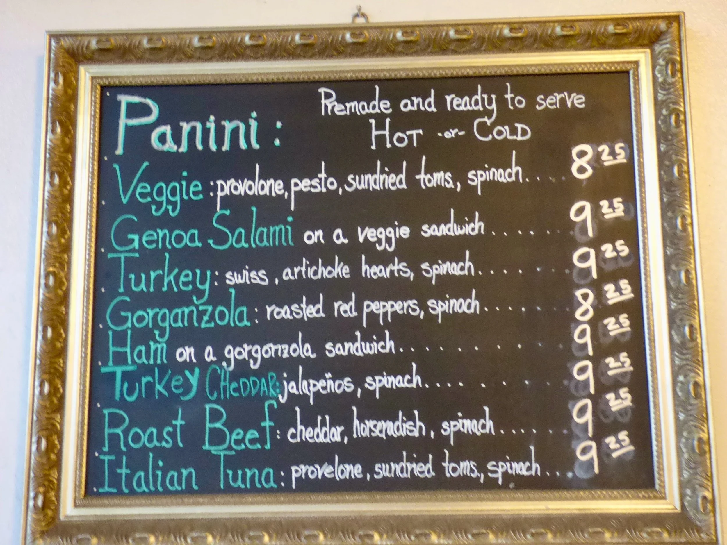Restaurant menu blackboard listing various types of panini sandwiches with ingredients and pricesat St. Mark's Coffeehouse & Bakery, Denver, CO.