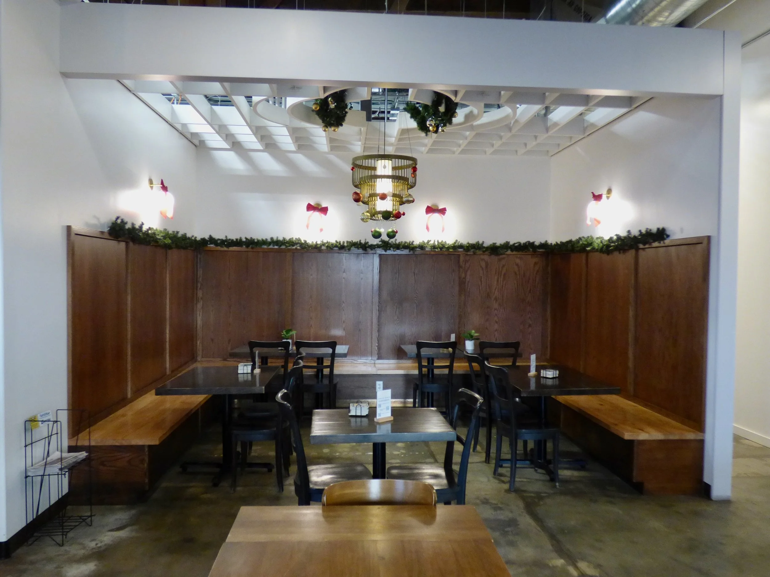 Empty restaurant corner decorated with Christmas garland, ornaments, and red bows, with tables and chairs at Cohesion Brewery, Denver, CO 80205.
