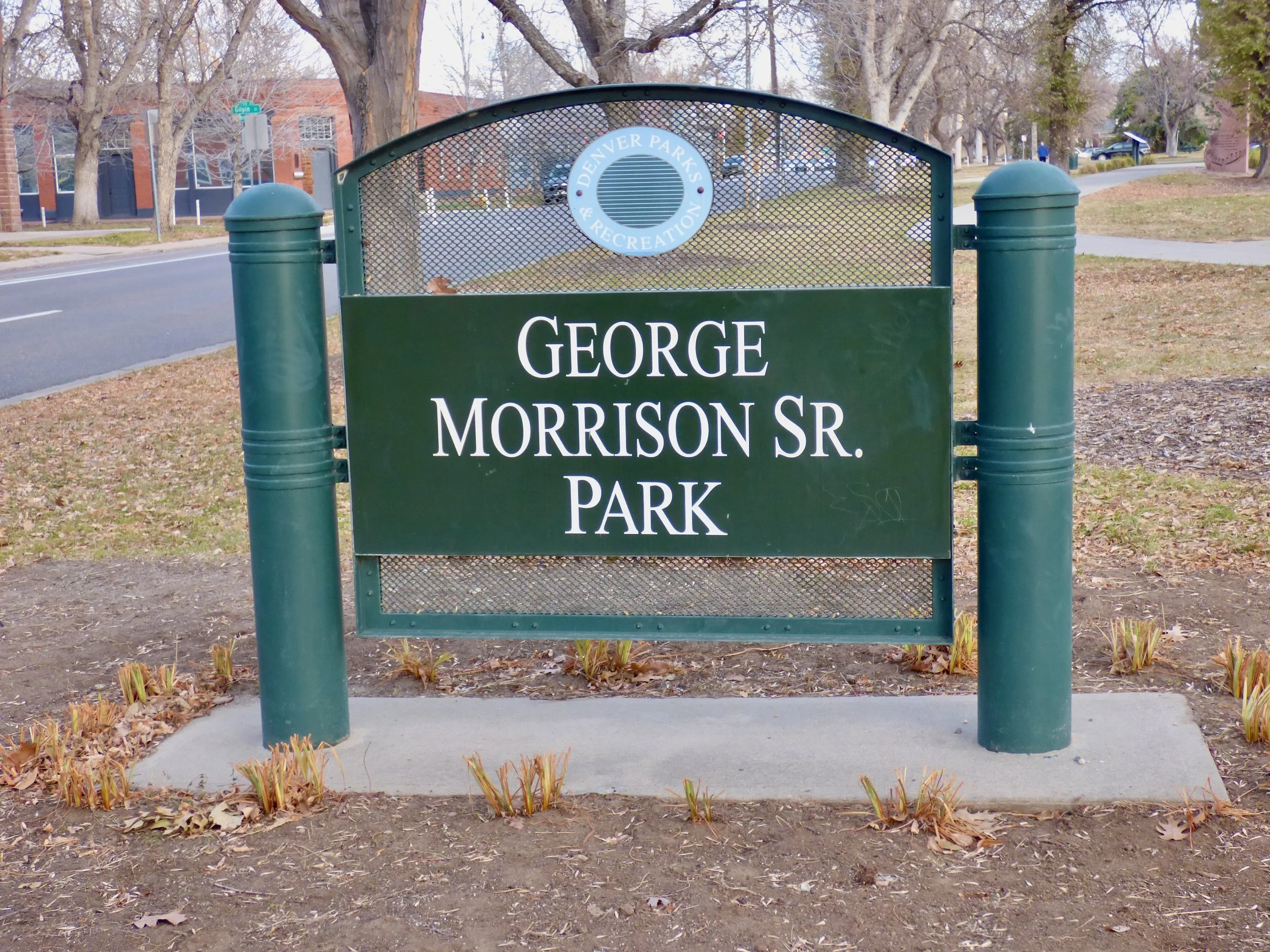Sign for George Morrison Sr. Park in Denver with trees and a sidewalk in the background at George Morrison Sr. Park, Denver, CO 80205.