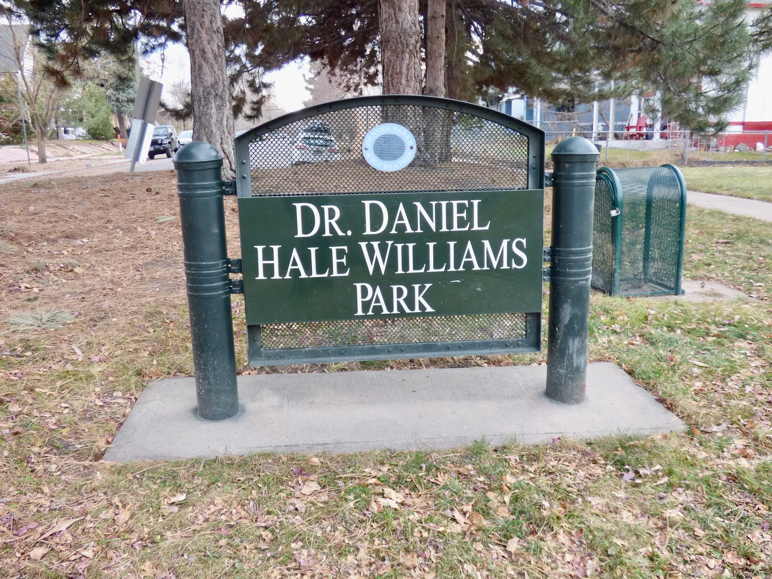 Sign for Dr. Daniel Hale Williams Park, with trees and a park bench in the background at Denver, CO 80205.