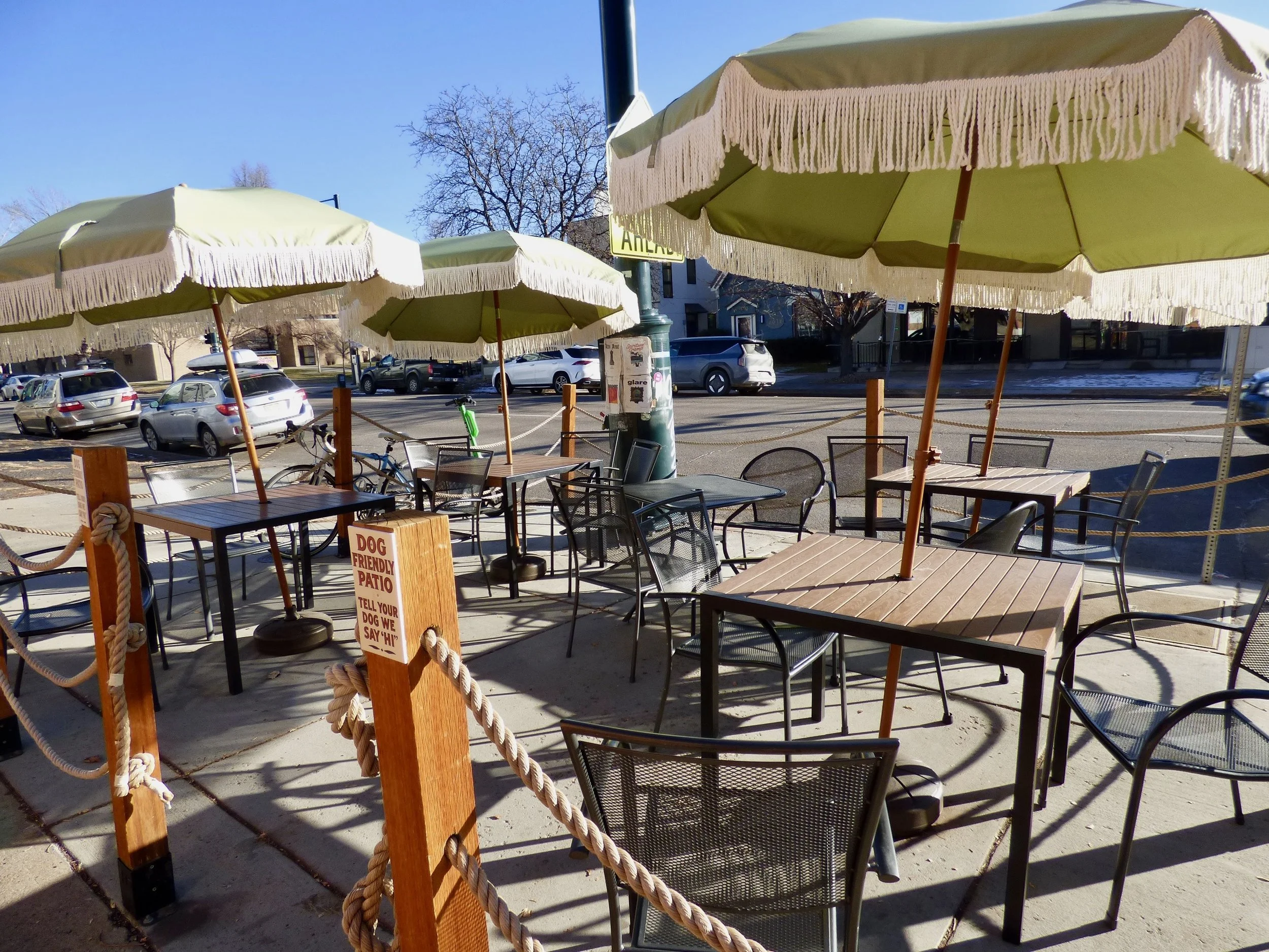Empty outdoor patio with tables, chairs, large umbrellas, and a sign that says 'Dog Friendly Patio'  at Weathervane Cafe, Denver, CO.