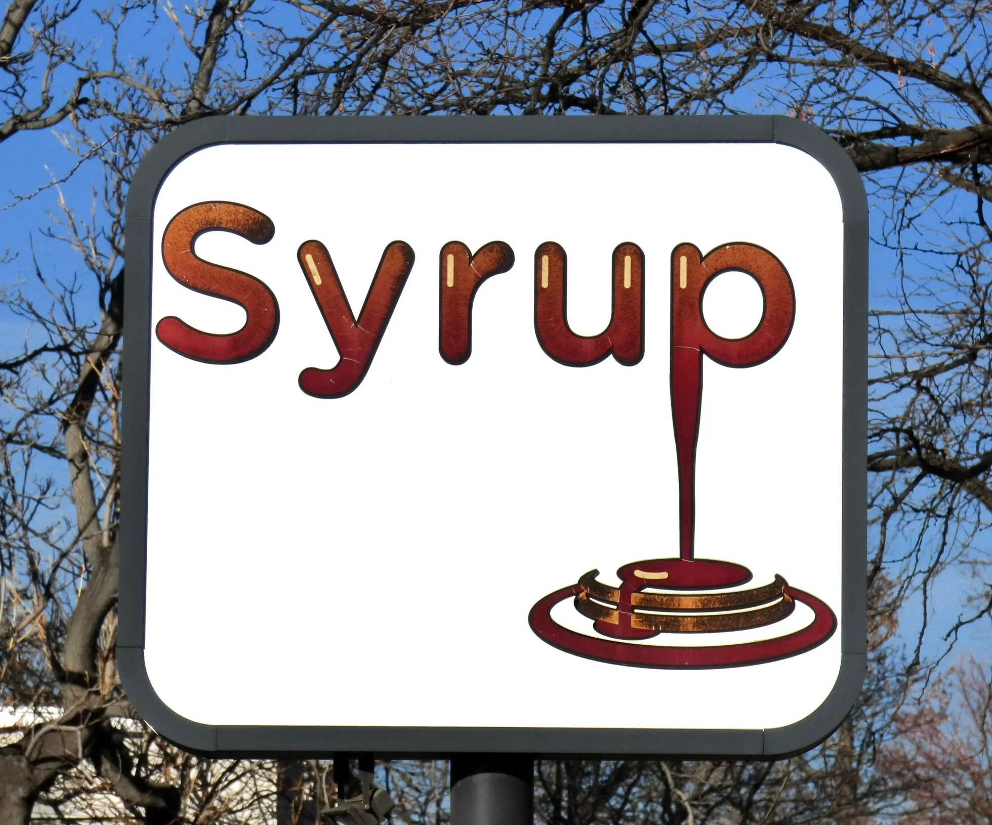 A sign with the word 'syrup' and an illustration of syrup pouring onto pancakes.