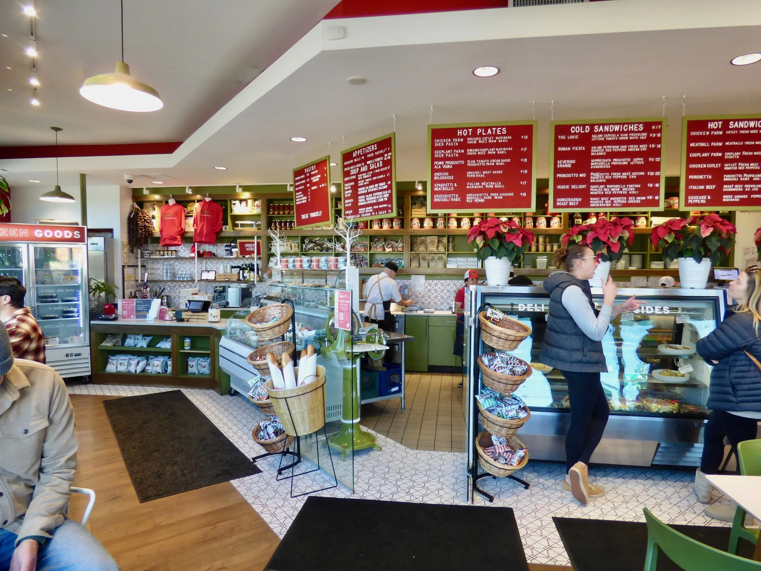 Inside a cafe or restaurant, with customers near the counter and display cases, menu boards hanging from the ceiling, and Christmas poinsettia decorations on the counter.