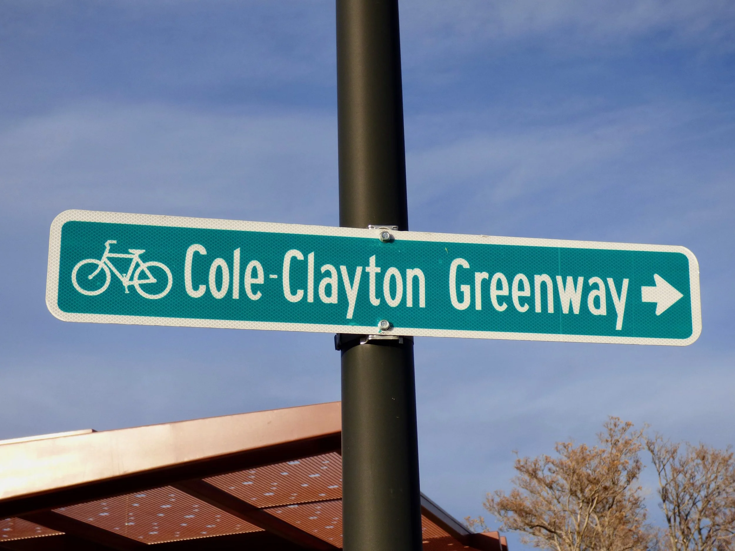 Street sign indicating the Cole-Clayton Greenway with a bicycle icon, pointing to the right, against a blue sky background in 39th Ave Greenway, Denver, CO 80205.
