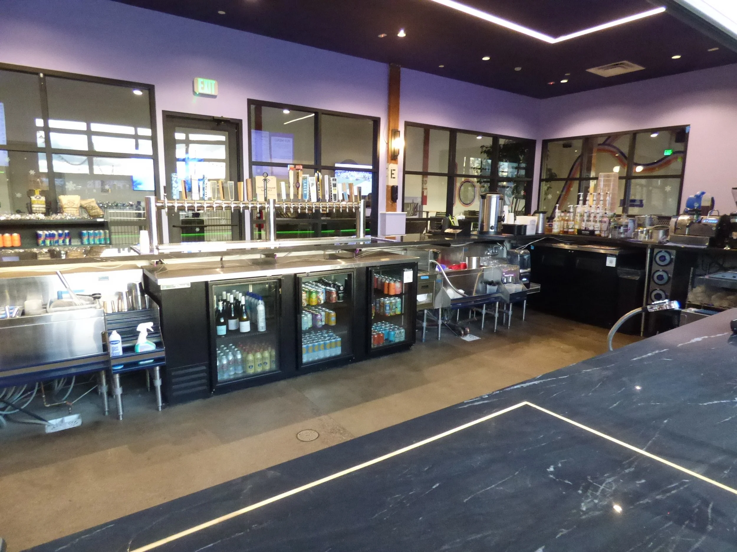 Interior view of a modern bar or restaurant counter with various beverage taps, cold storage, and coffee brewing equipment at Skiptown, Denver, CO 80205.