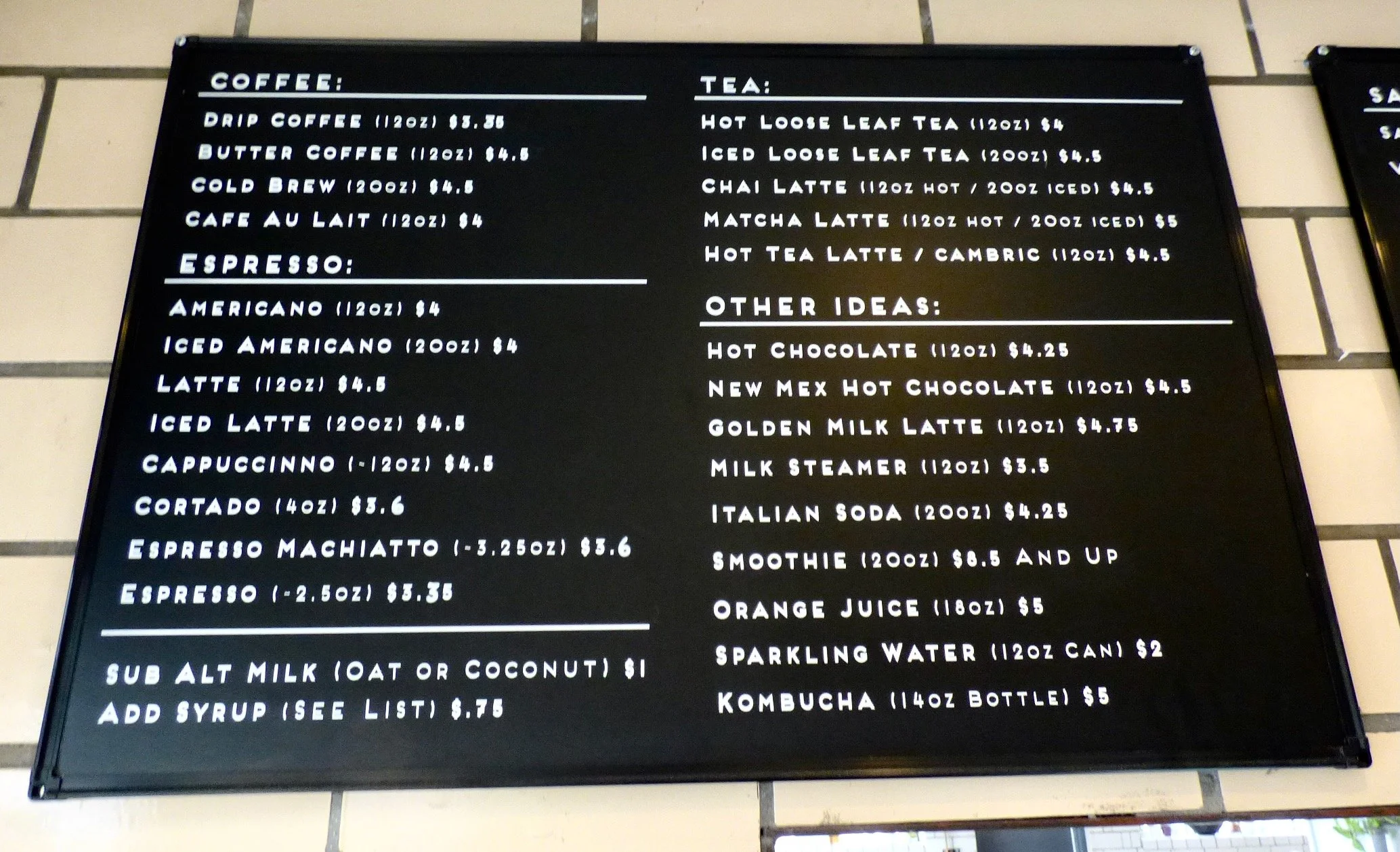 Black menu board with white text displaying coffee, espresso, tea, and other drink options and prices.