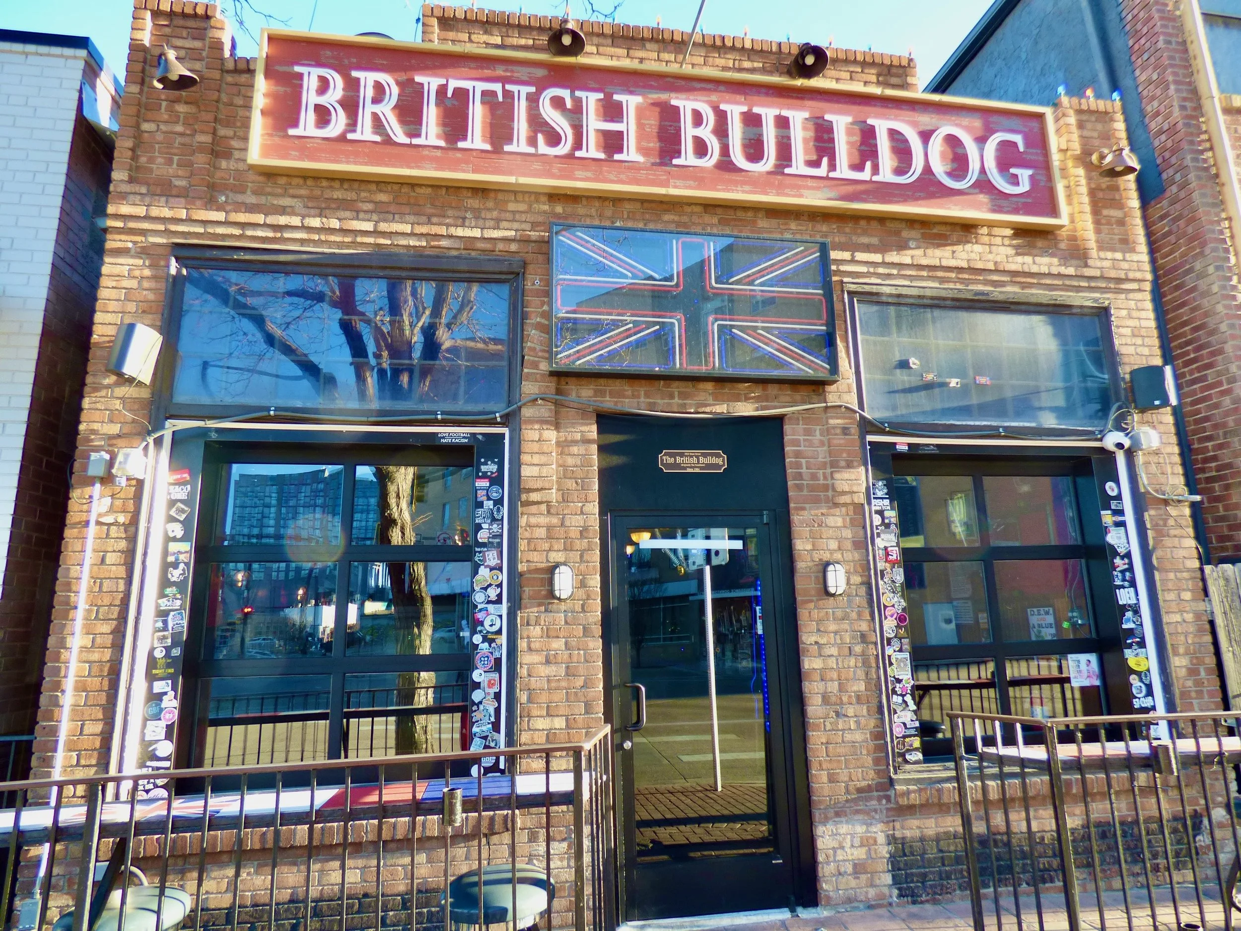 Brick building with a sign reading 'British Bulldog' and a stylized Union Jack flag on a screen above the door at The British Bulldog, Denver, CO 80205.