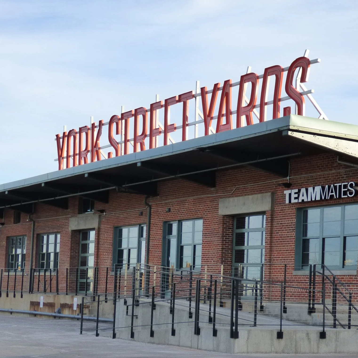 Exterior of a brick building with a marquee sign on roof reading 'YORK STREET VARRS'. Ramps and stairs lead up to entrances, and a sign on the wall reads 'TEAM MATES'.