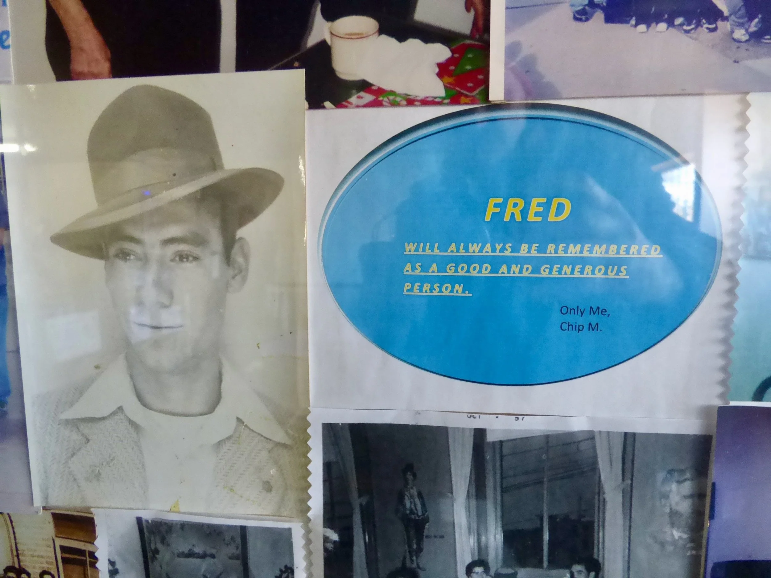 A black-and-white photograph of a young man wearing a hat and a collared shirt. Additionally, there is a blue paper with yellow and blue text that reads: "FRED will always be remembered as a good and generous person. Only Me, Chip M."
