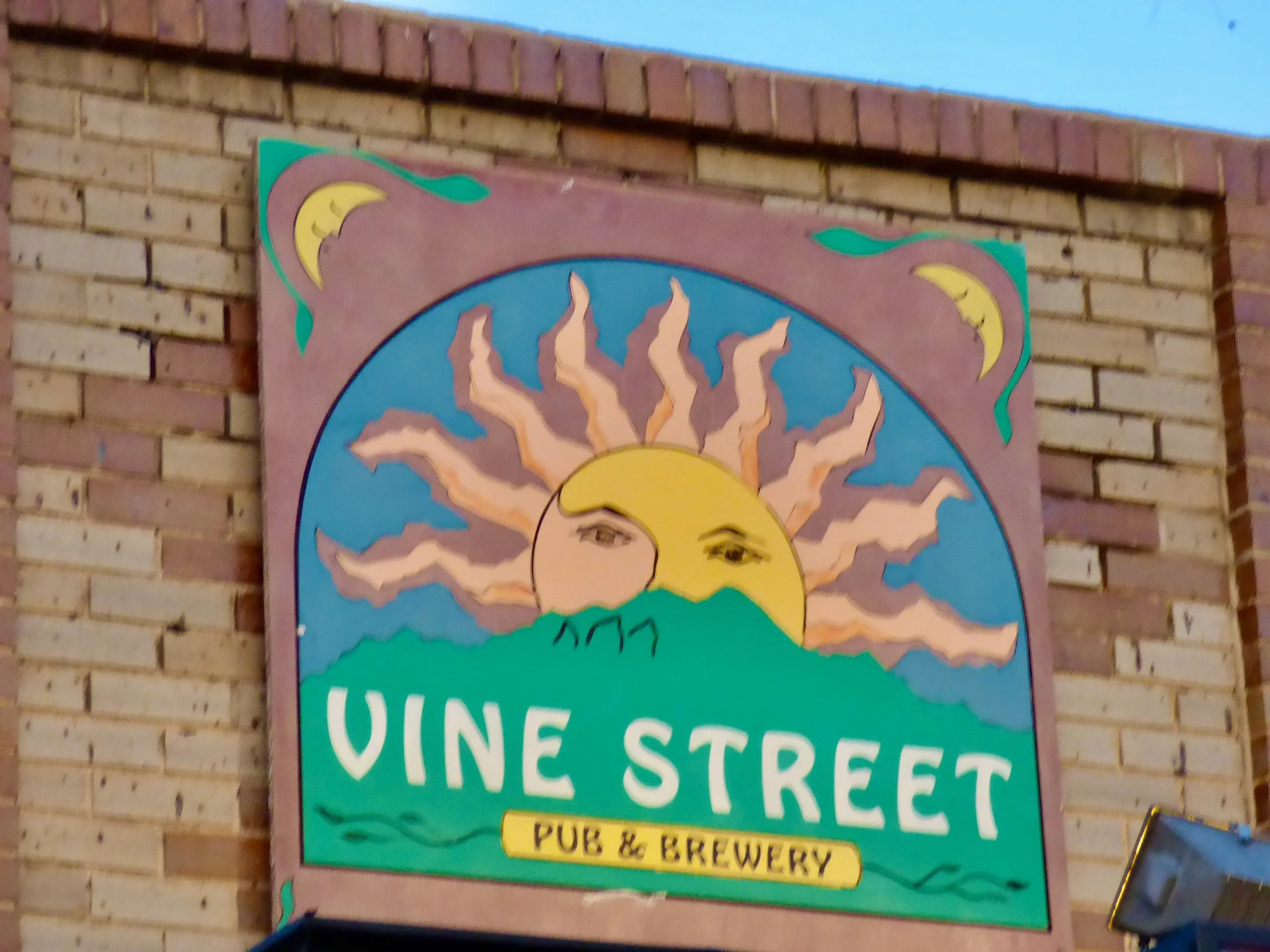 Sign for Vine Street Pub & Brewery featuring a sun with a human face, mountains, and two crescent moons at the corners at Vine Street Pub, Denver, CO.