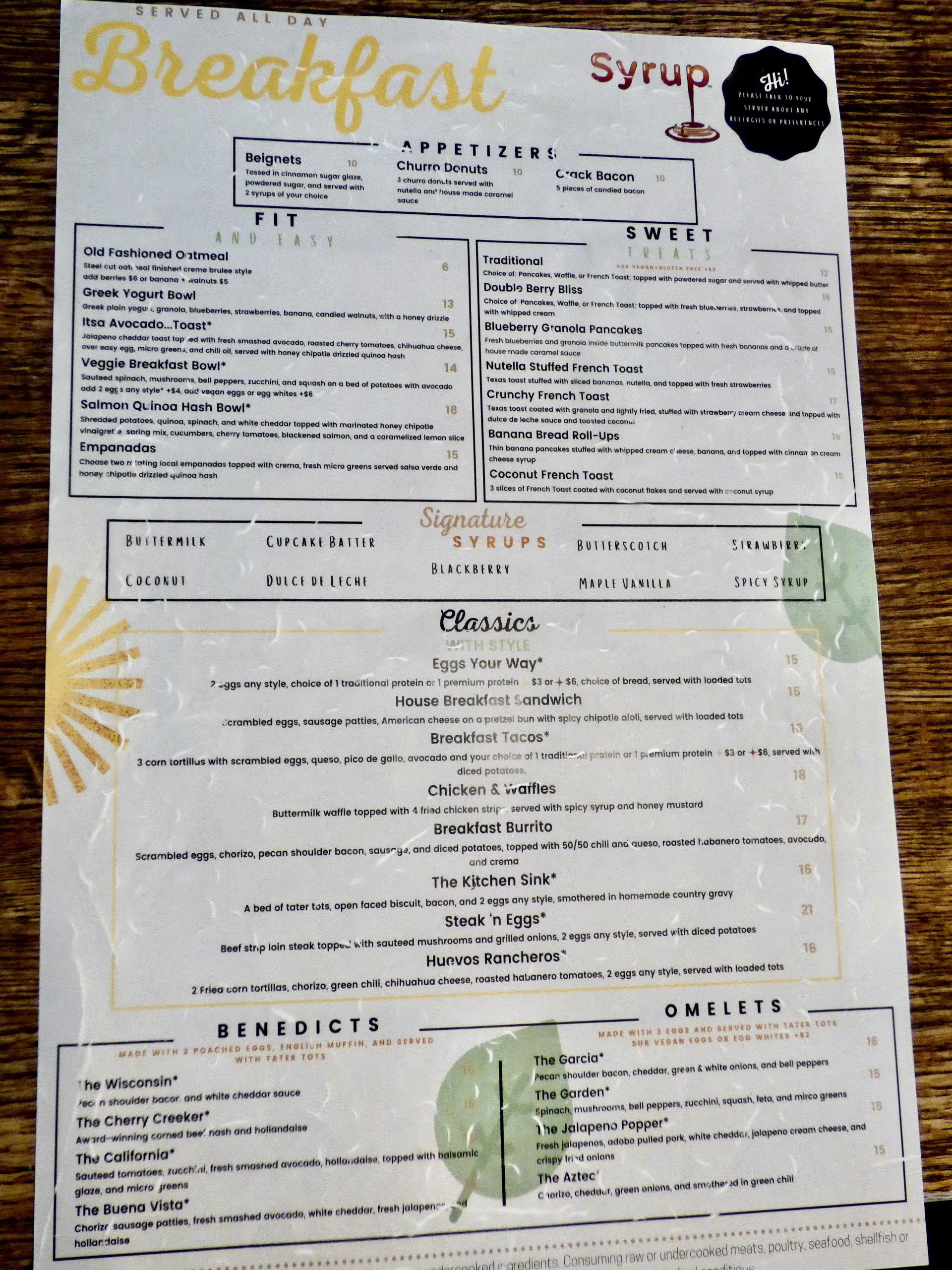 Menu for a breakfast restaurant featuring appetizers, sweet treats, classics, benedicts, omelets, and signature syrups.