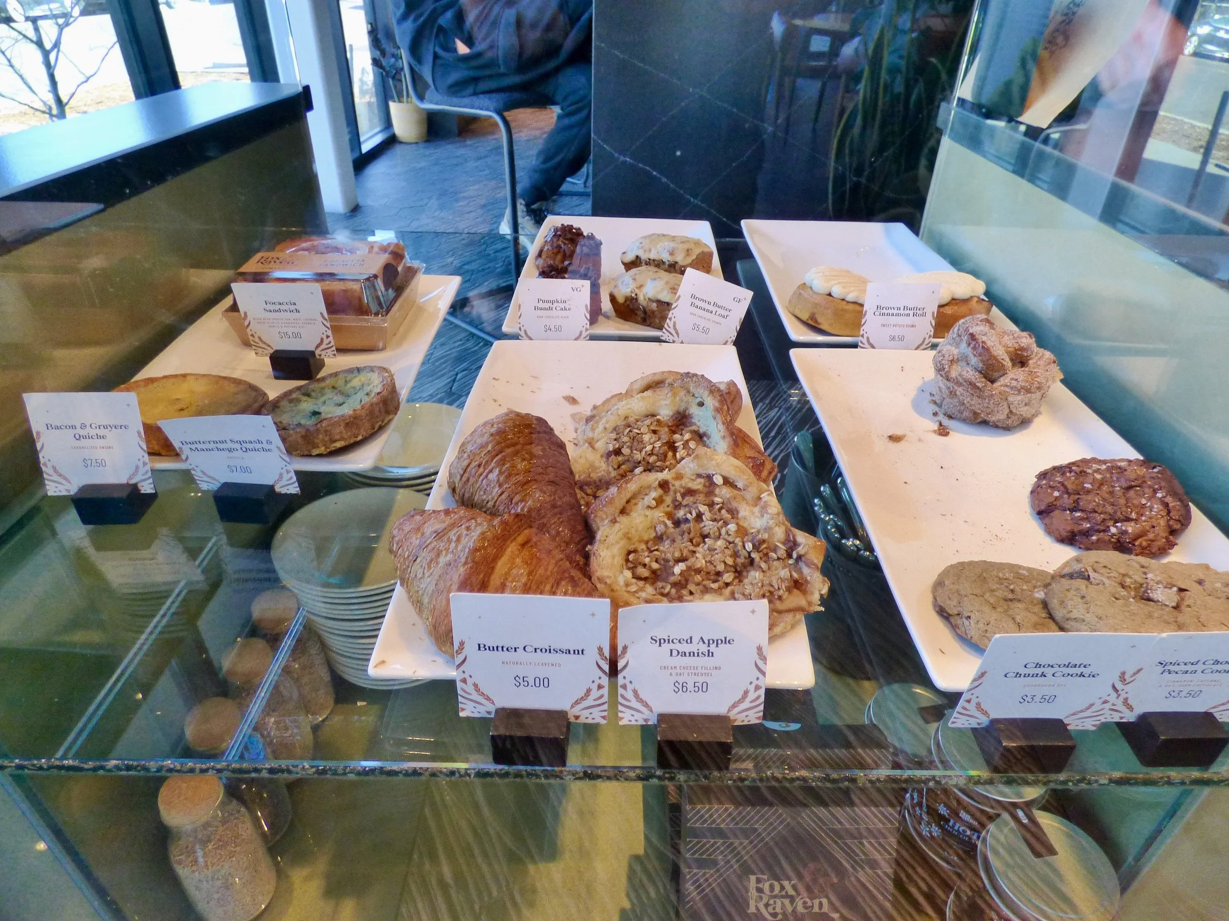 Display case containing various baked goods including croissants, cookies, muffins, and coffee cakes at Corvus Coffee Roasters, Denver, CO 80205.