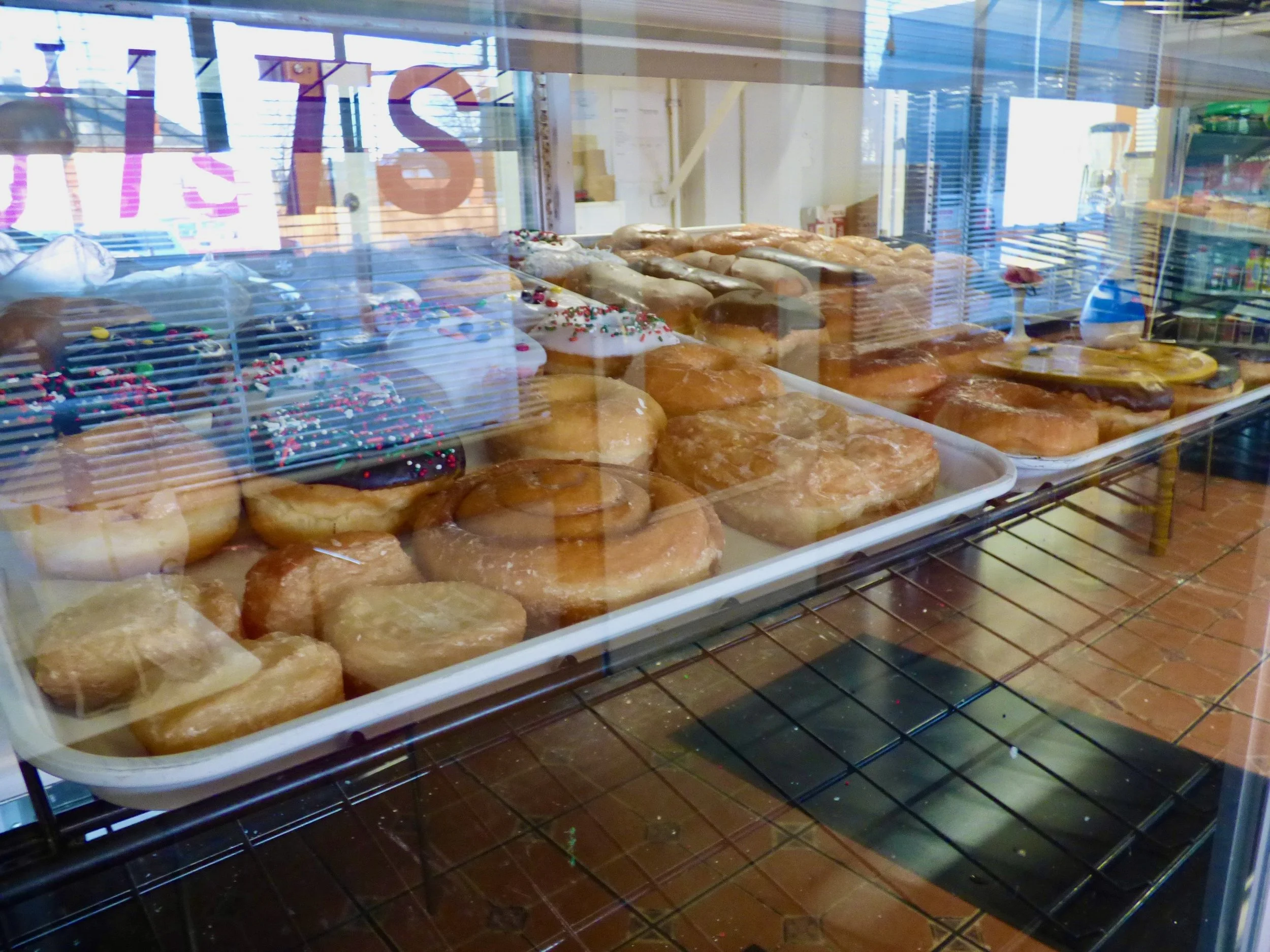 Display case filled with assorted donuts, including chocolate glazed with sprinkles and powdered sugar donuts at PF Donut Shop, Denver, CO 80205.