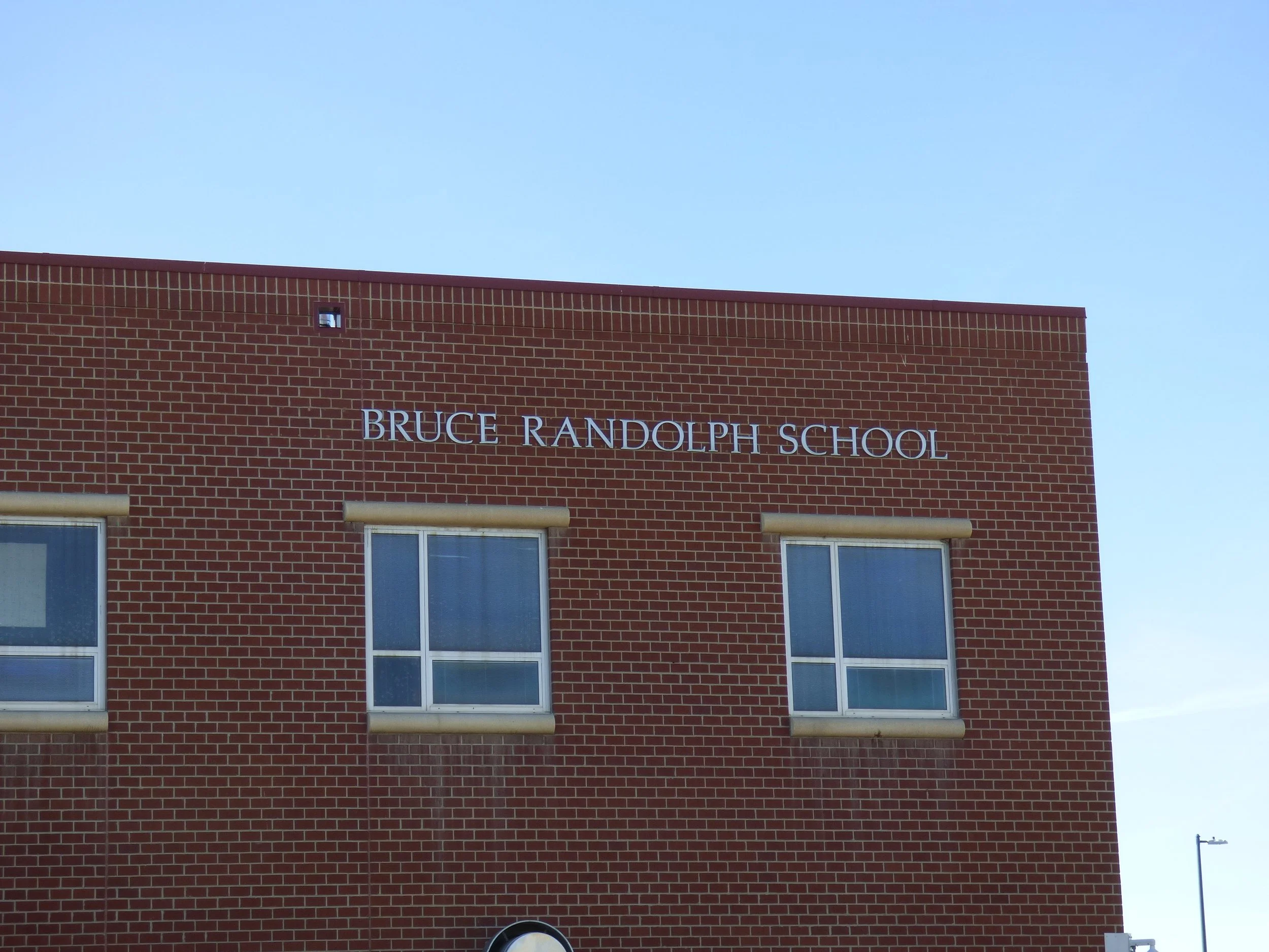 Red brick building with sign reading 'Bruce Randolph School' and two windows beneath.