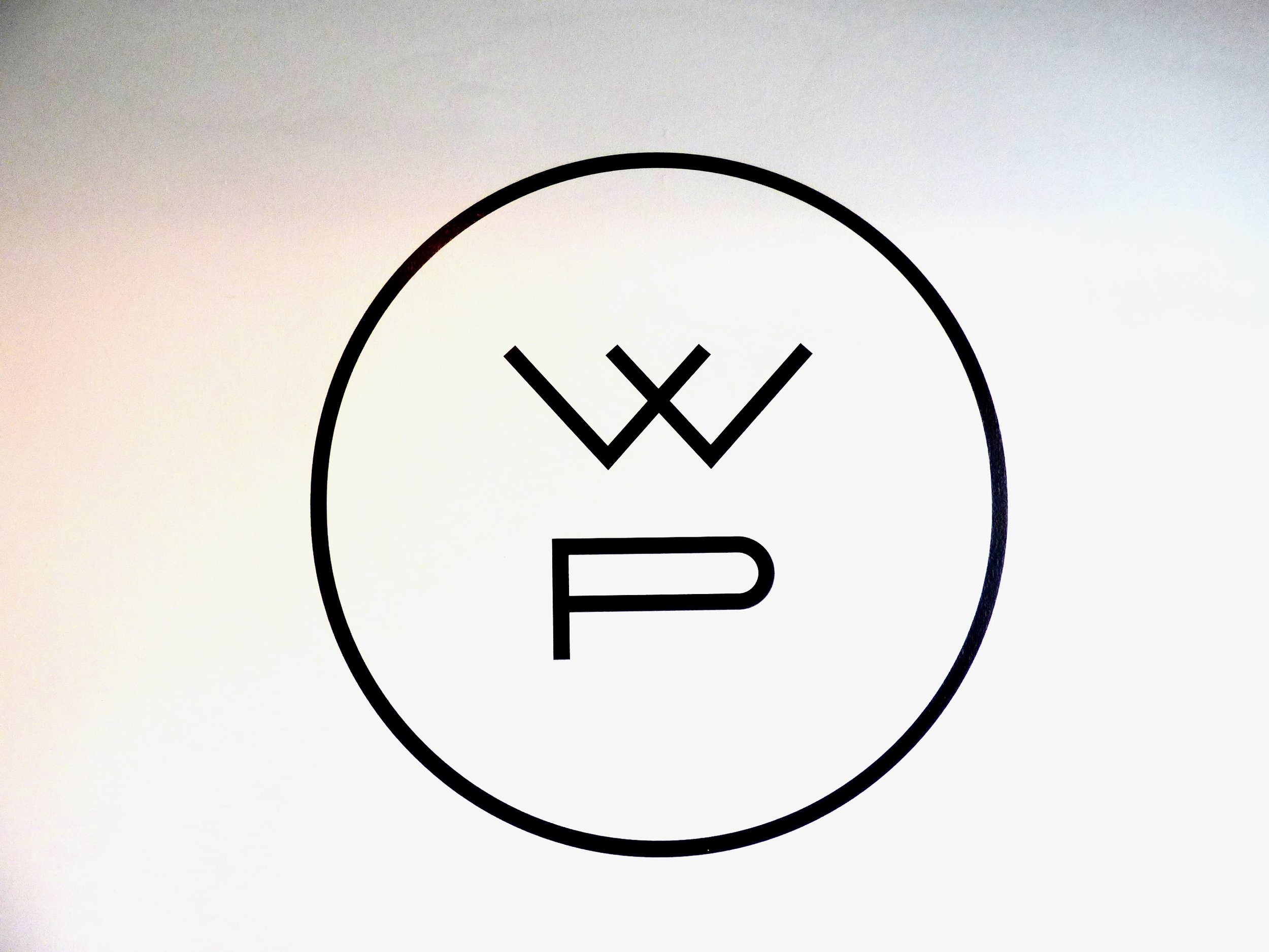 A circular logo with a stylized face, featuring two 'W' shapes for eyes and a 'P' shape for a mouth, enclosed in a black circle.