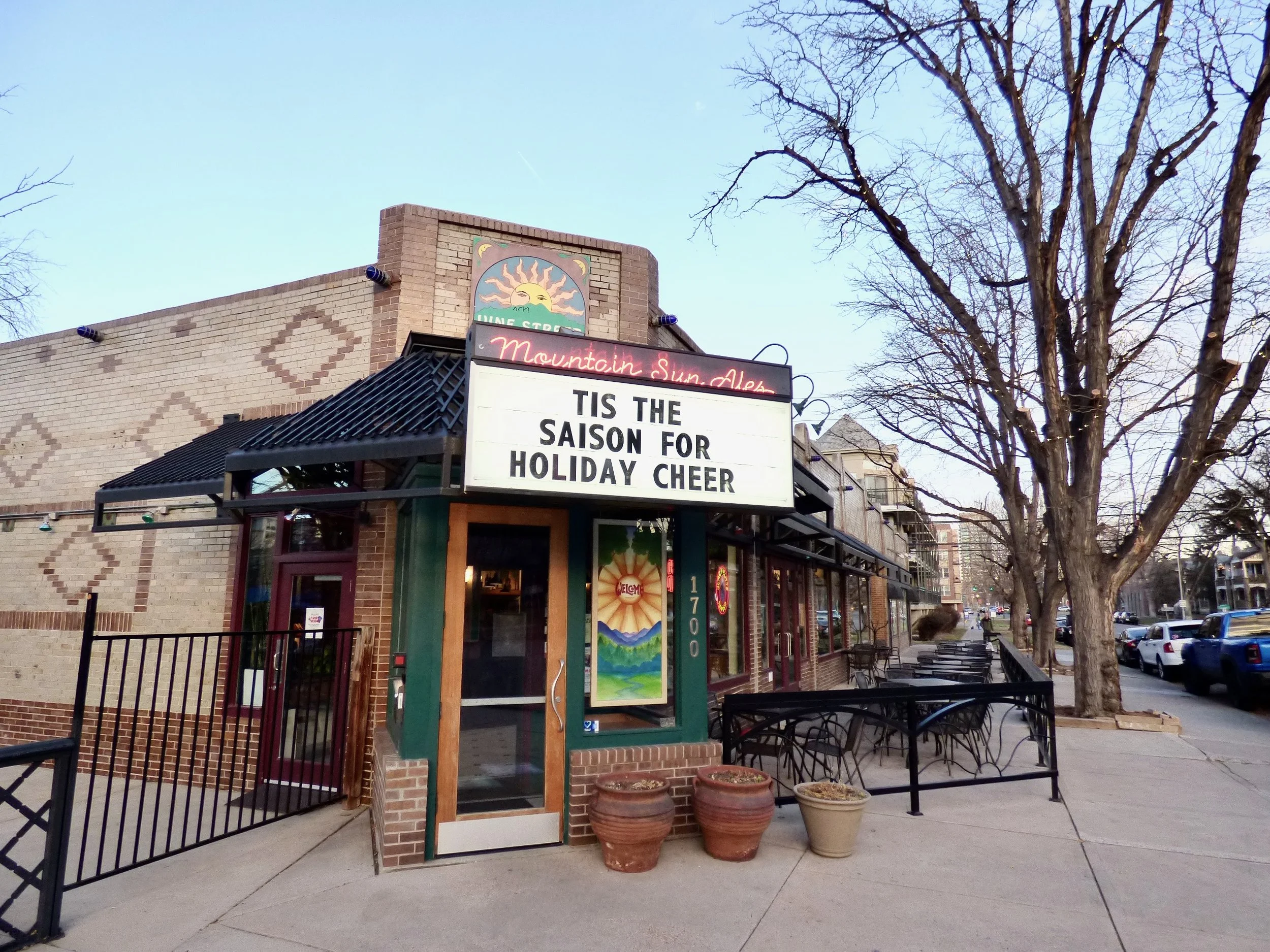 Exterior of a restaurant called Mountain Sun Ale with a large sign on the front saying 'TIS THE SAISON FOR HOLIDAY CHEER' during late afternoon or early evening at Vine Street Pub, Denver, CO.