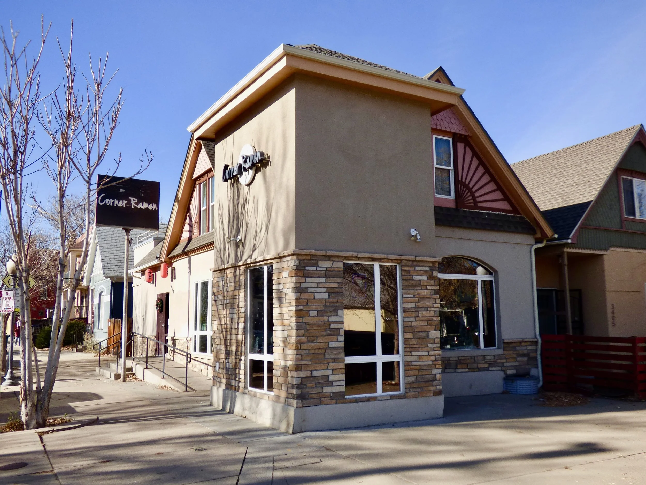 Building on the corner with a sign that says 'Corner Ramen', featuring a mix of stone and stucco exterior, with a restaurant logo sign and adjacent sidewalk with leafless trees.